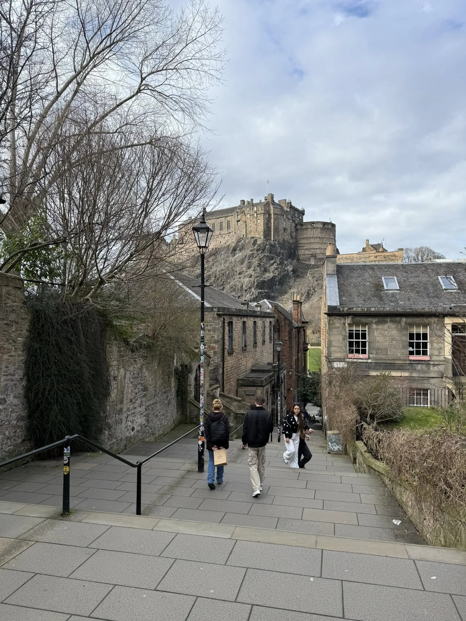 Street scene in Edinburgh Old Town with historic buildings, people walking, and Edinburgh Castle visible in the background