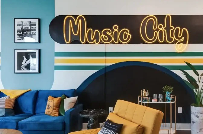 Yellow "Music City" neon sign mounted above a blue sofa in a contemporary living room.