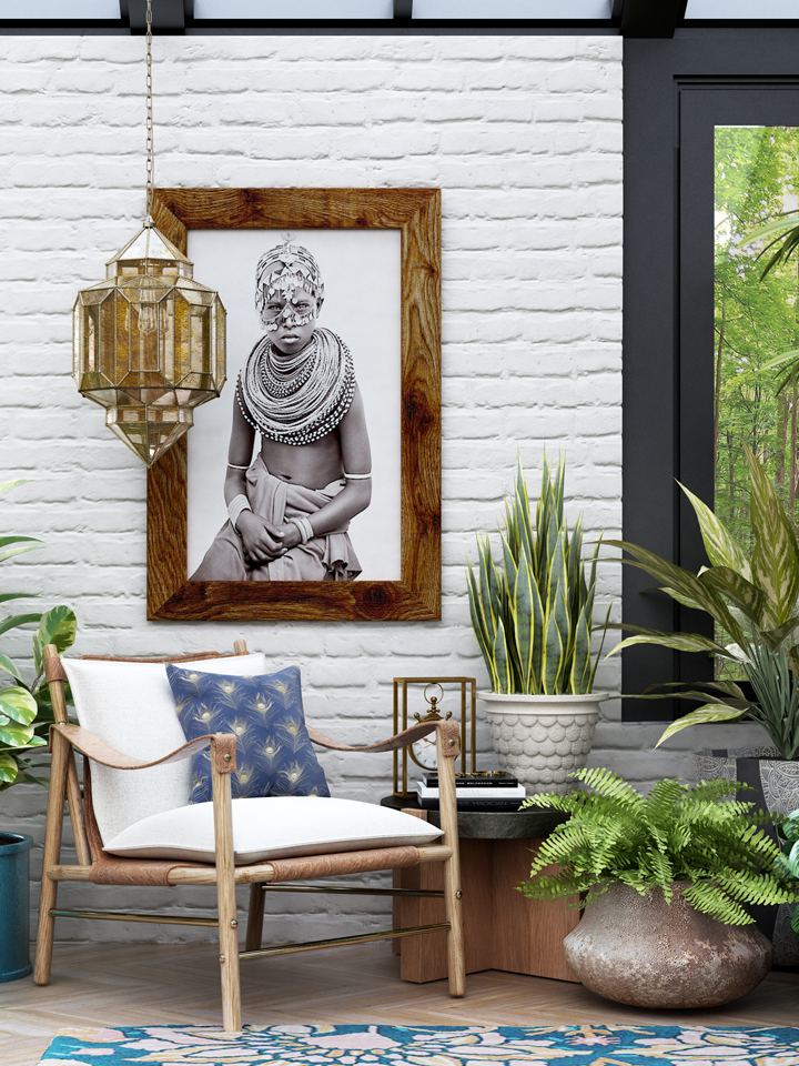 Eclectic sunroom wall decor with framed global portrait art, brass lantern pendant, white brick wall, accent chair, and layered plants, designed by virtual interior designer Joshua Jones of JJones Design Co.