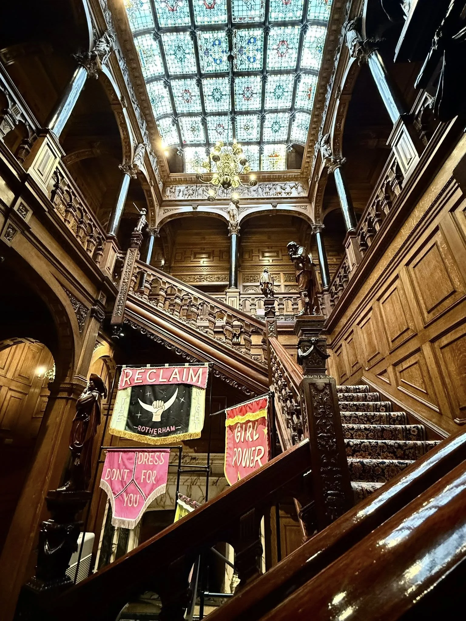 Interior of Two Temple Place in London showing carved wood staircase, detailed paneling, and stained glass ceiling above
