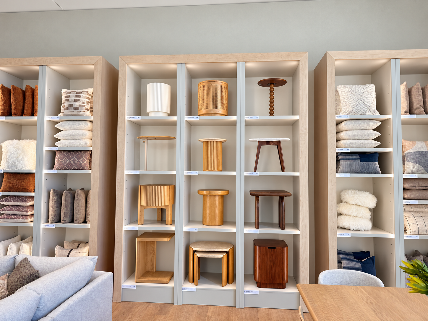 Side tables displayed on central shelves, with textured and patterned decorative pillows arranged on shelving on both sides.