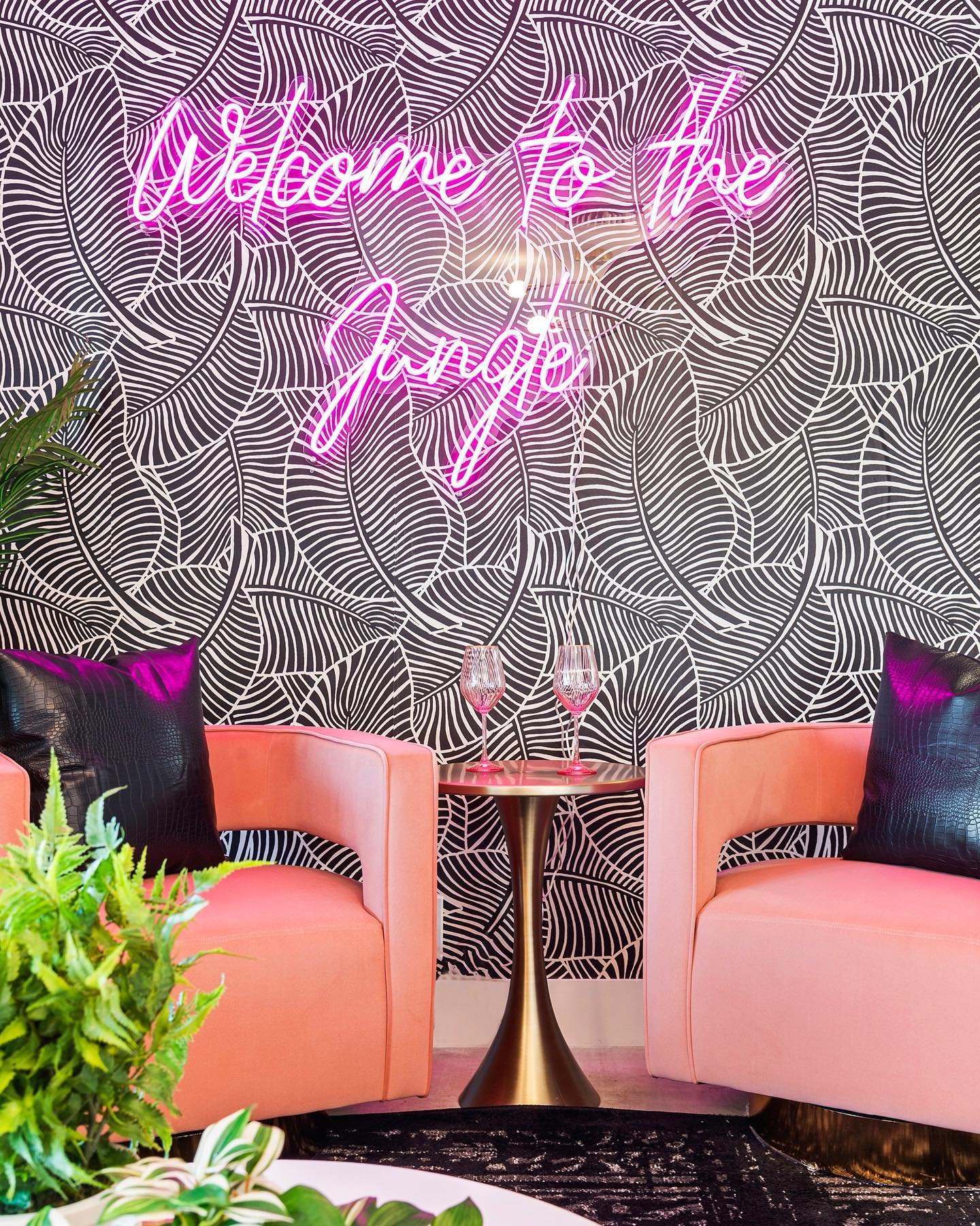 Green "Welcome to the Jungle" neon sign mounted above pink accent chairs in a tropical-inspired lounge.