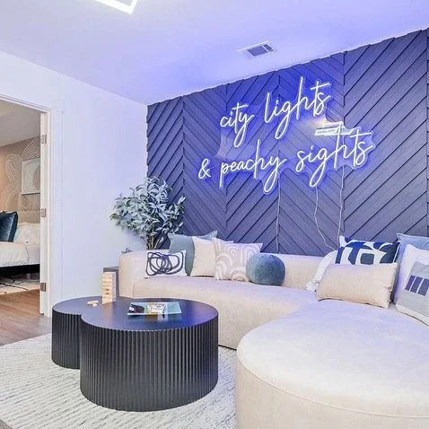 White "City Lights & Peachy Sights" neon sign mounted on a blue herringbone accent wall in a living room.