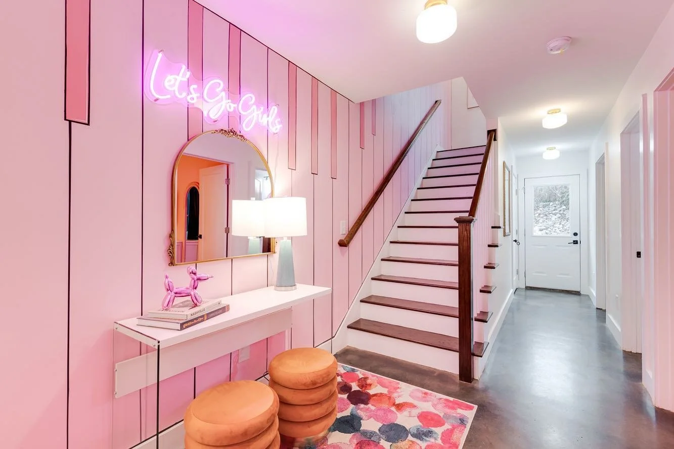 Pink "Let's Go Girls" neon sign displayed in a colorful entryway with pink walls and decorative lighting.
