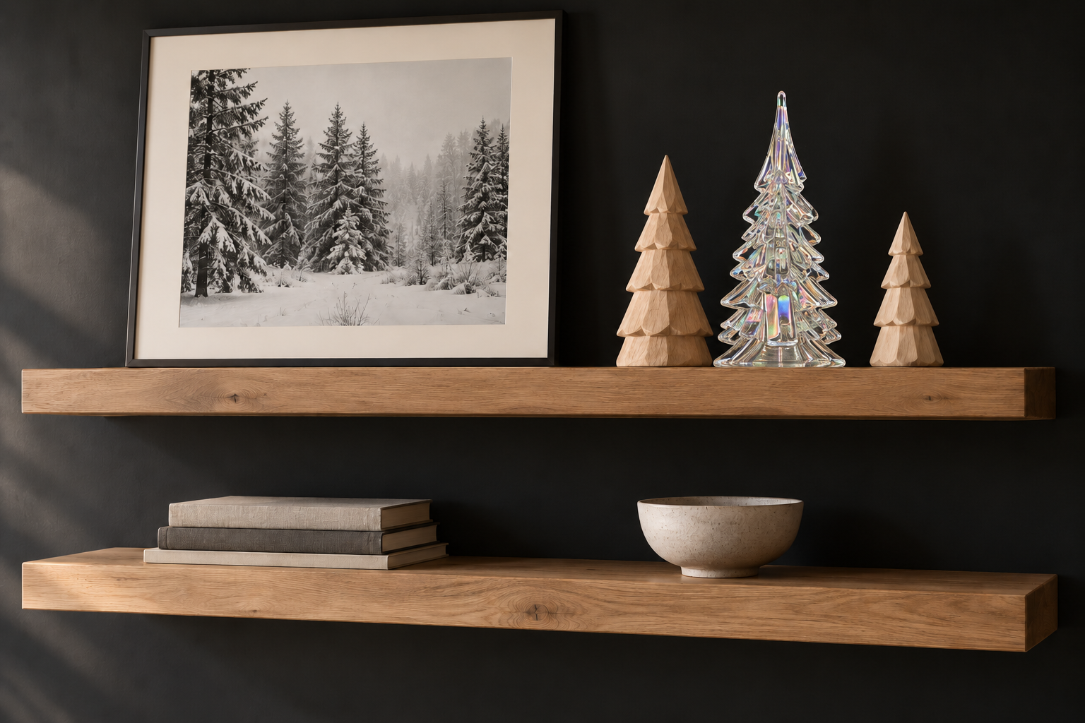 Oak floating shelves against a black wall, with framed snowy forest photography and a tall glass Christmas tree between two shorter carved wood trees; books and a ceramic bowl sit below.
