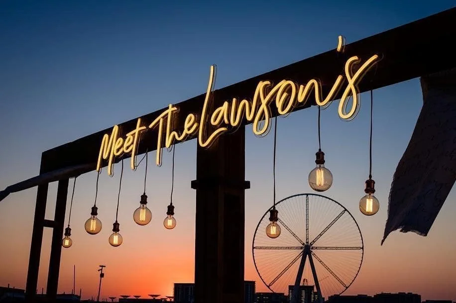 Large custom "Meet the Lawsons" neon sign displayed against a greenery backdrop at an event venue.