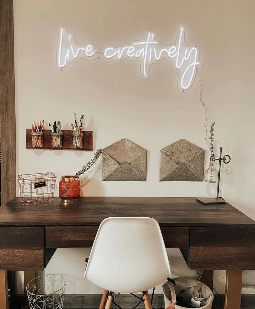 White "Live Creatively" neon sign mounted above a desk in a modern home office.
