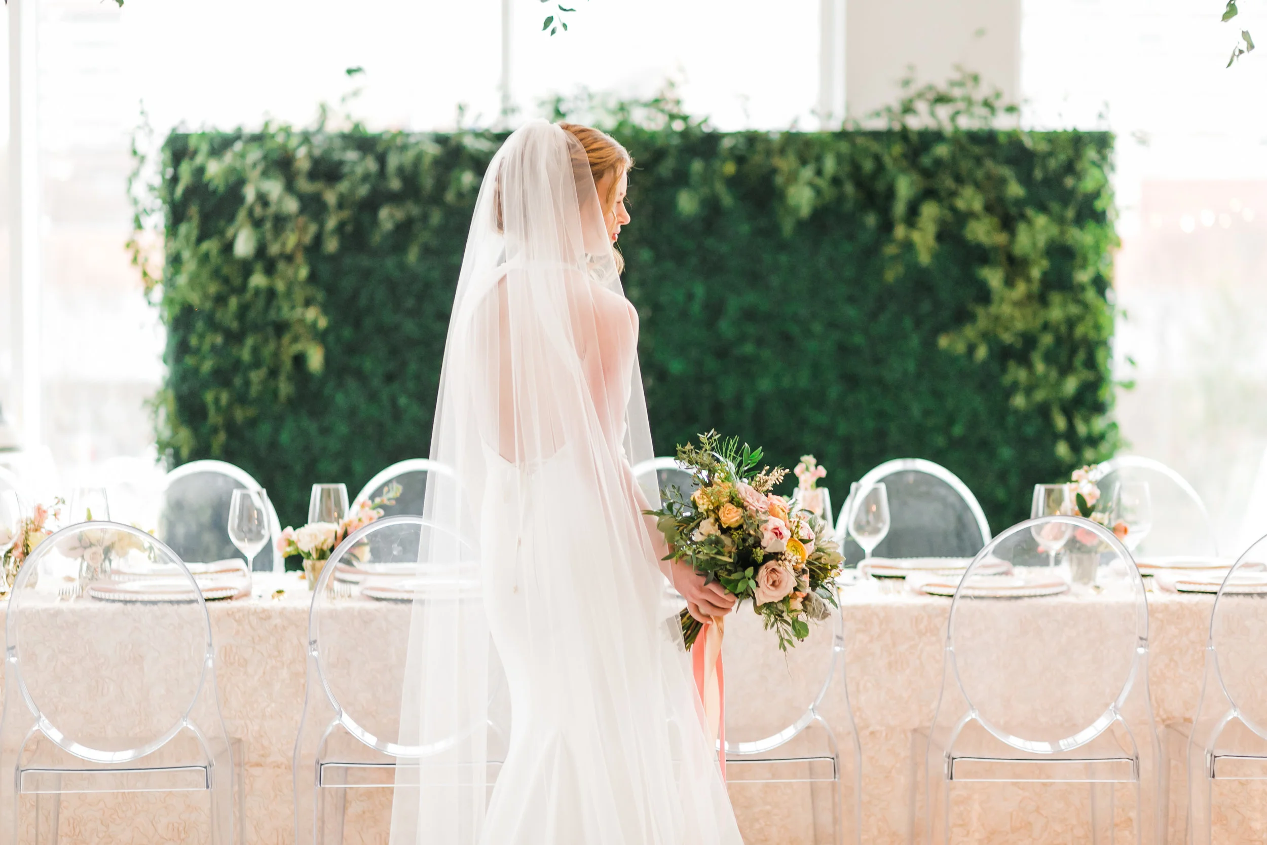 bride in front of reception table with greenery wall indoor