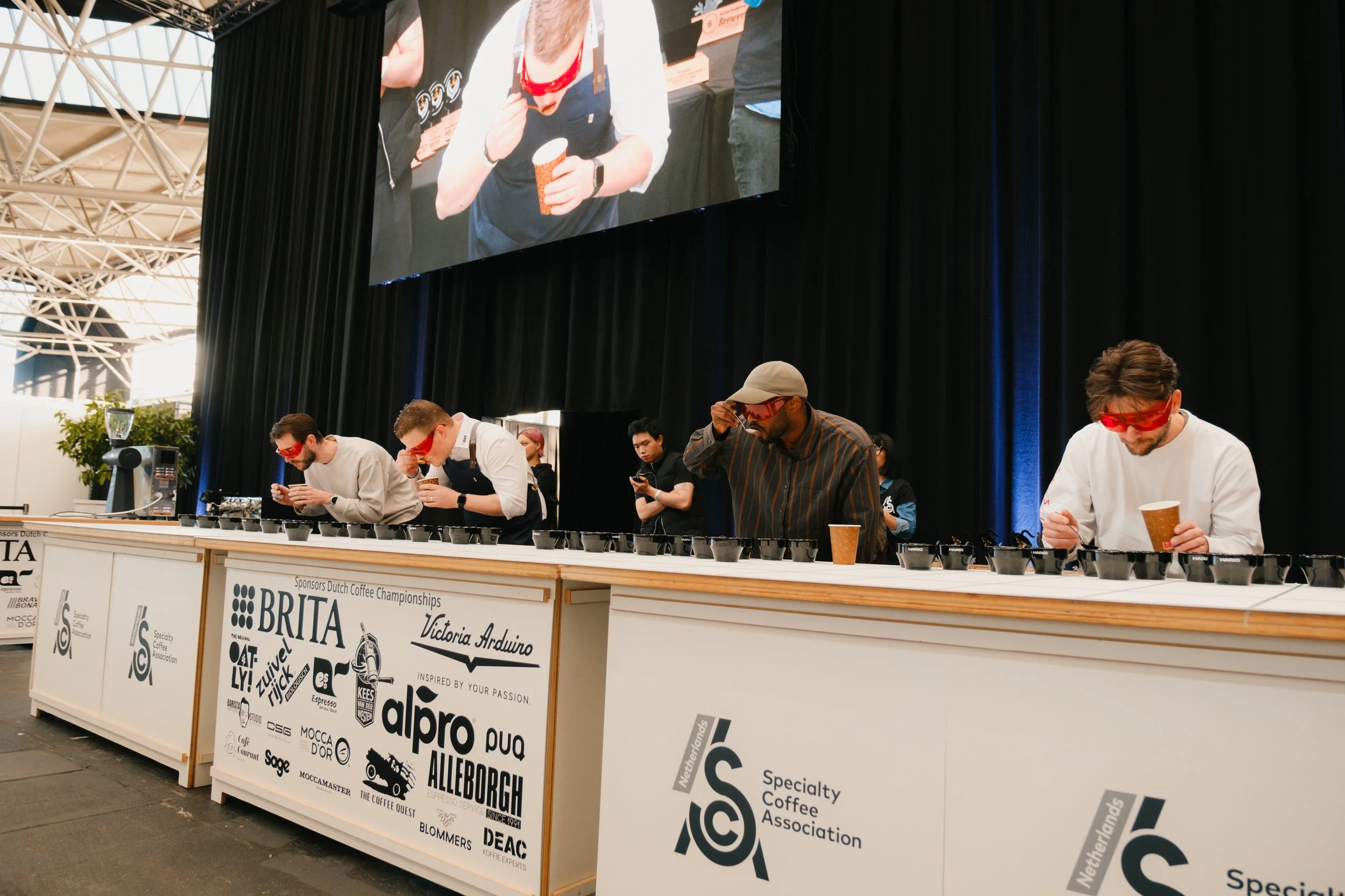 Four people tasting teas with a spoon. They wear red glasses