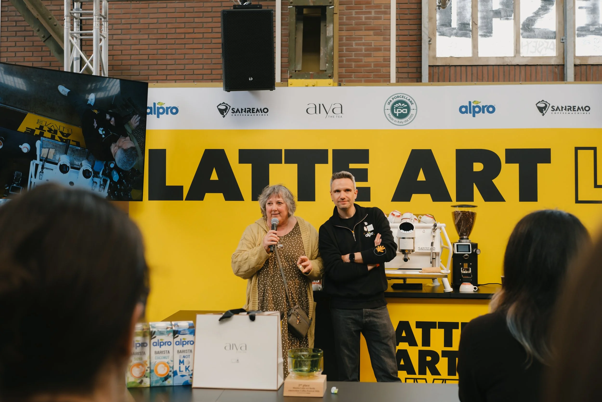 Two people in front of the space prepared for the Matcha Lattte conpettion. One of them is talking with a microphone