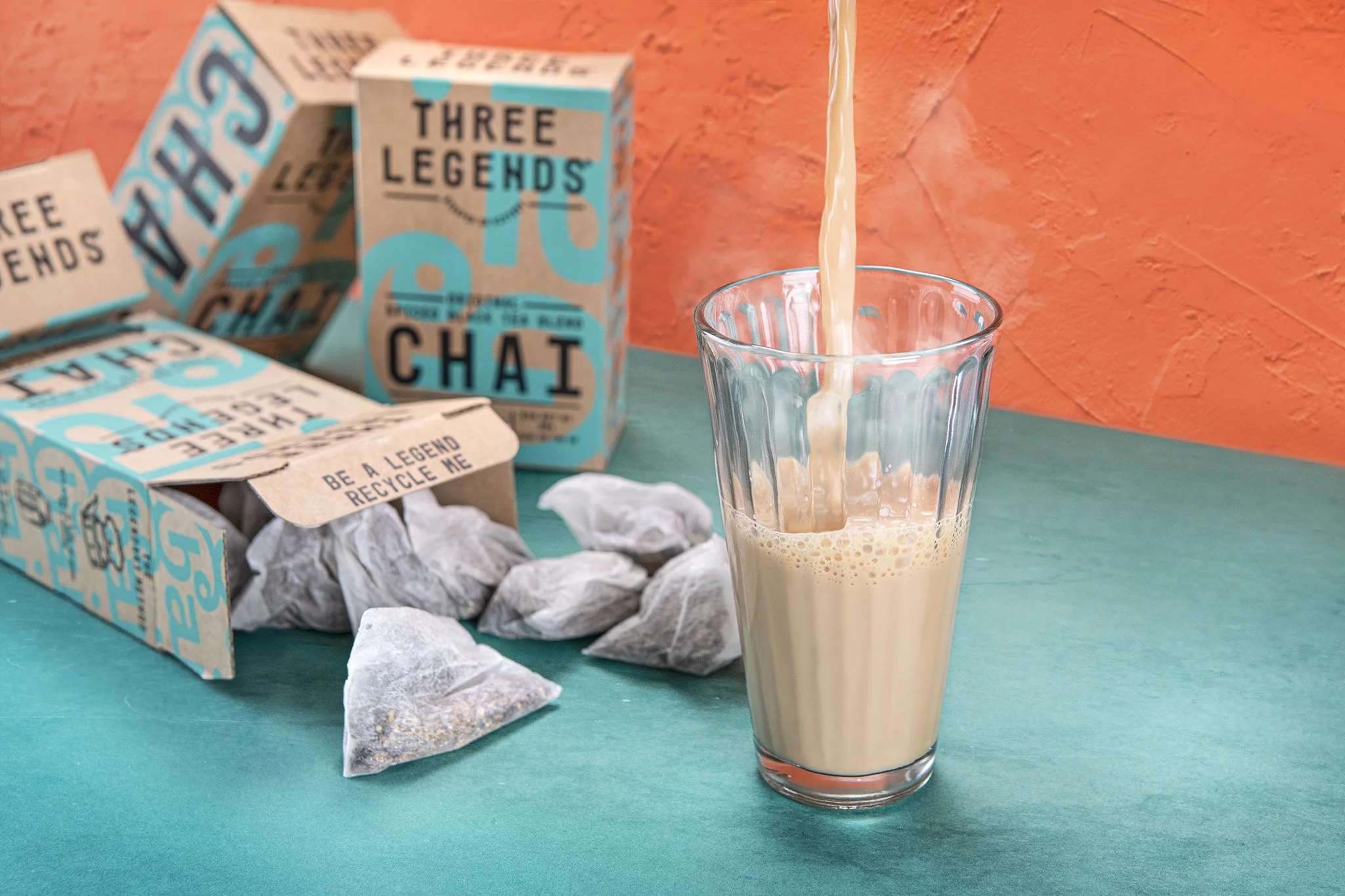 A glass is filling with chai. There are some tea bags coming out from one a packaging