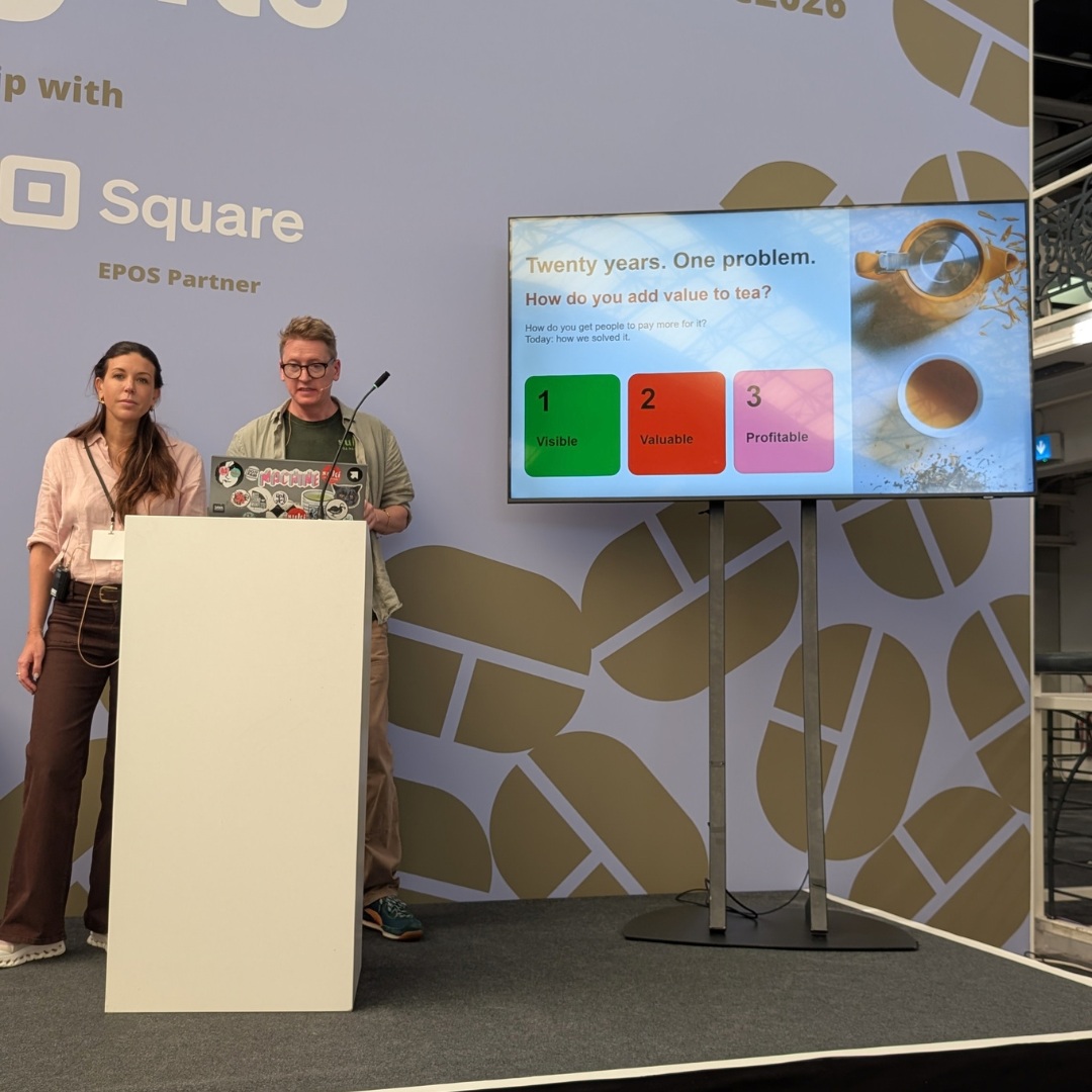 Two people on a stage standing behind a lectern with a screen on their left