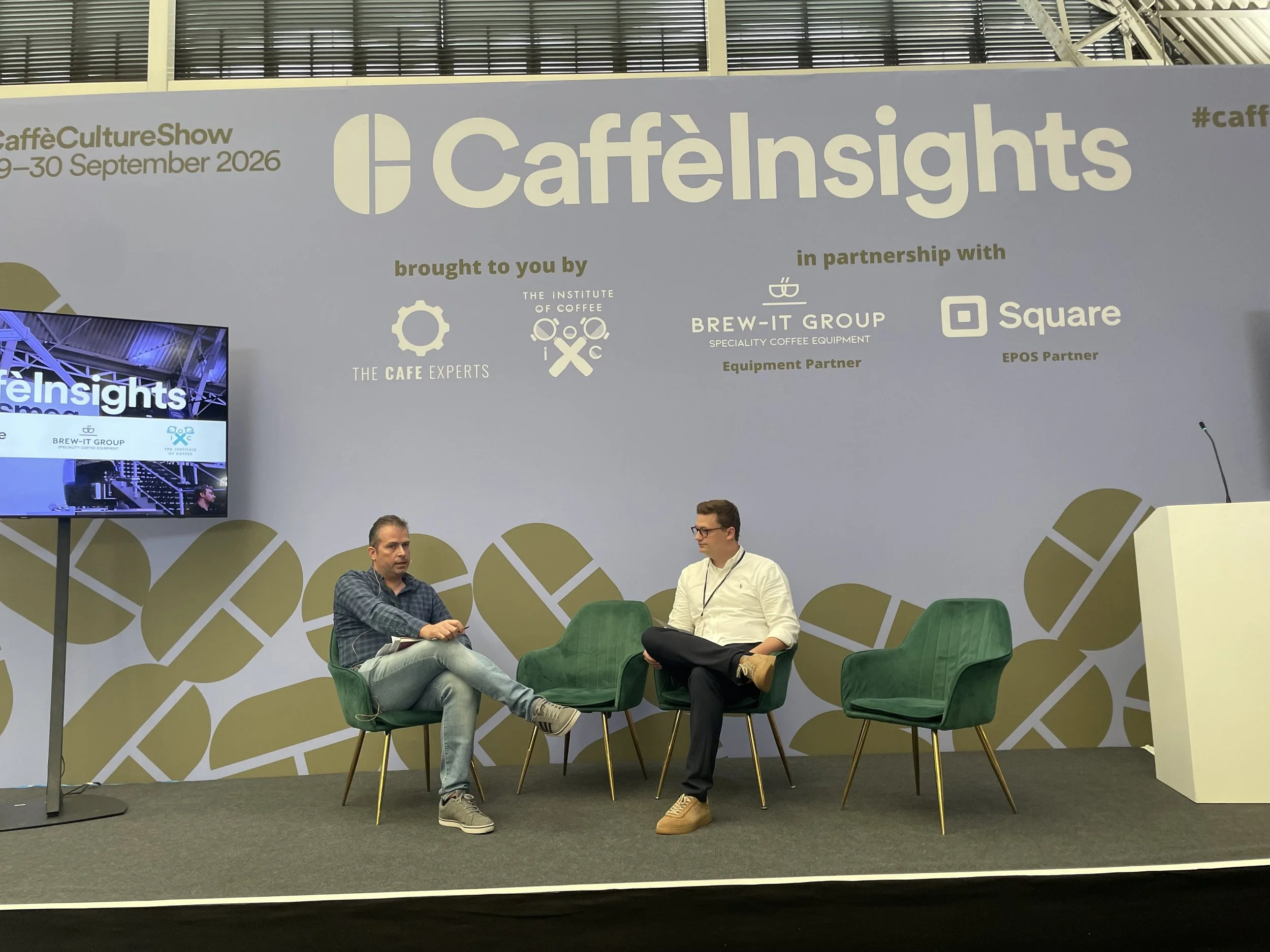 Two people seating on a stage. They are talking
