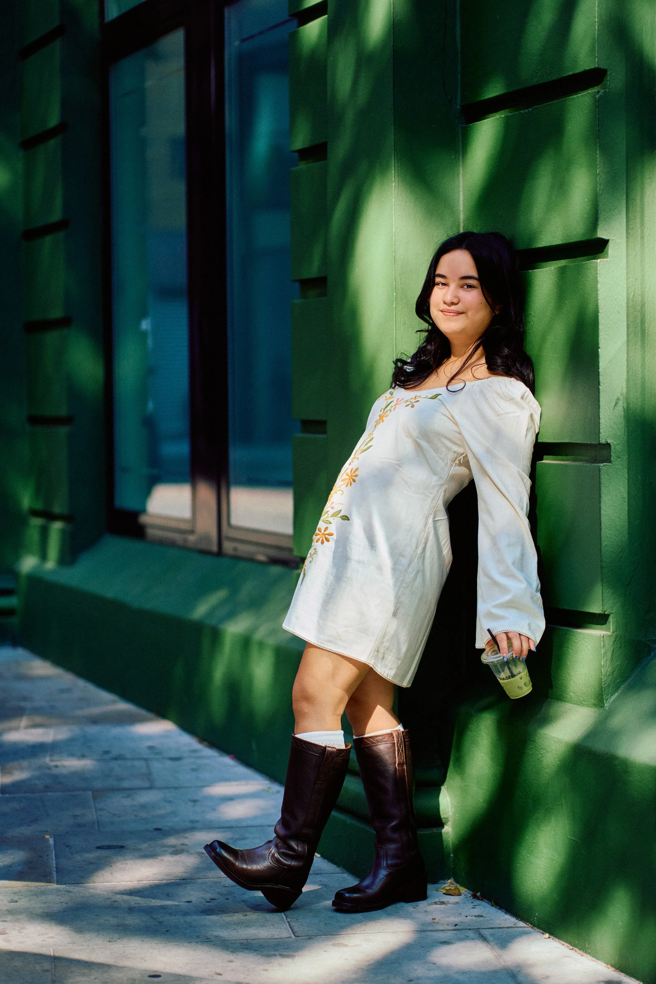 Young woman in a white embroidered dress leaning against a green door in Covent Garden
