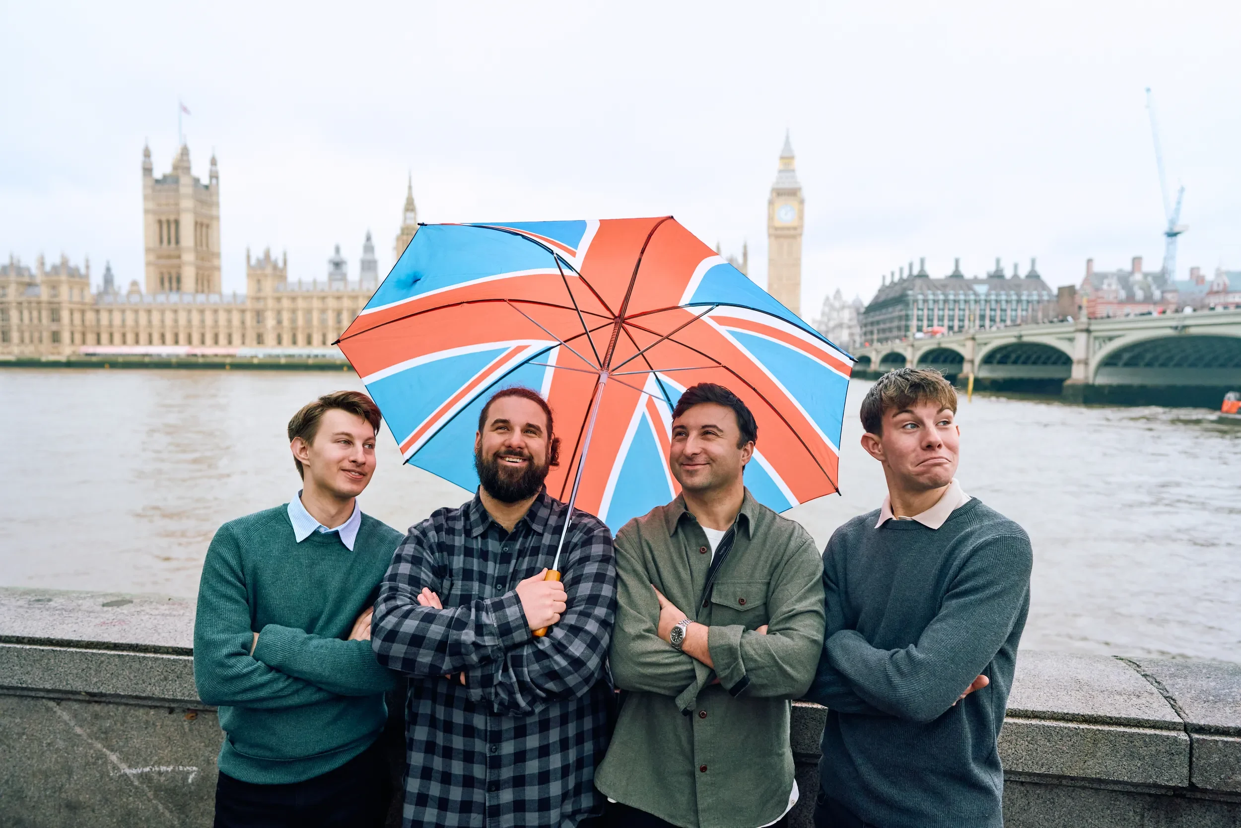 Four friends posing with a Union Jack umbrella on the South Bank with Big Ben and Westminster Bridge behind them during a group photoshoot in London