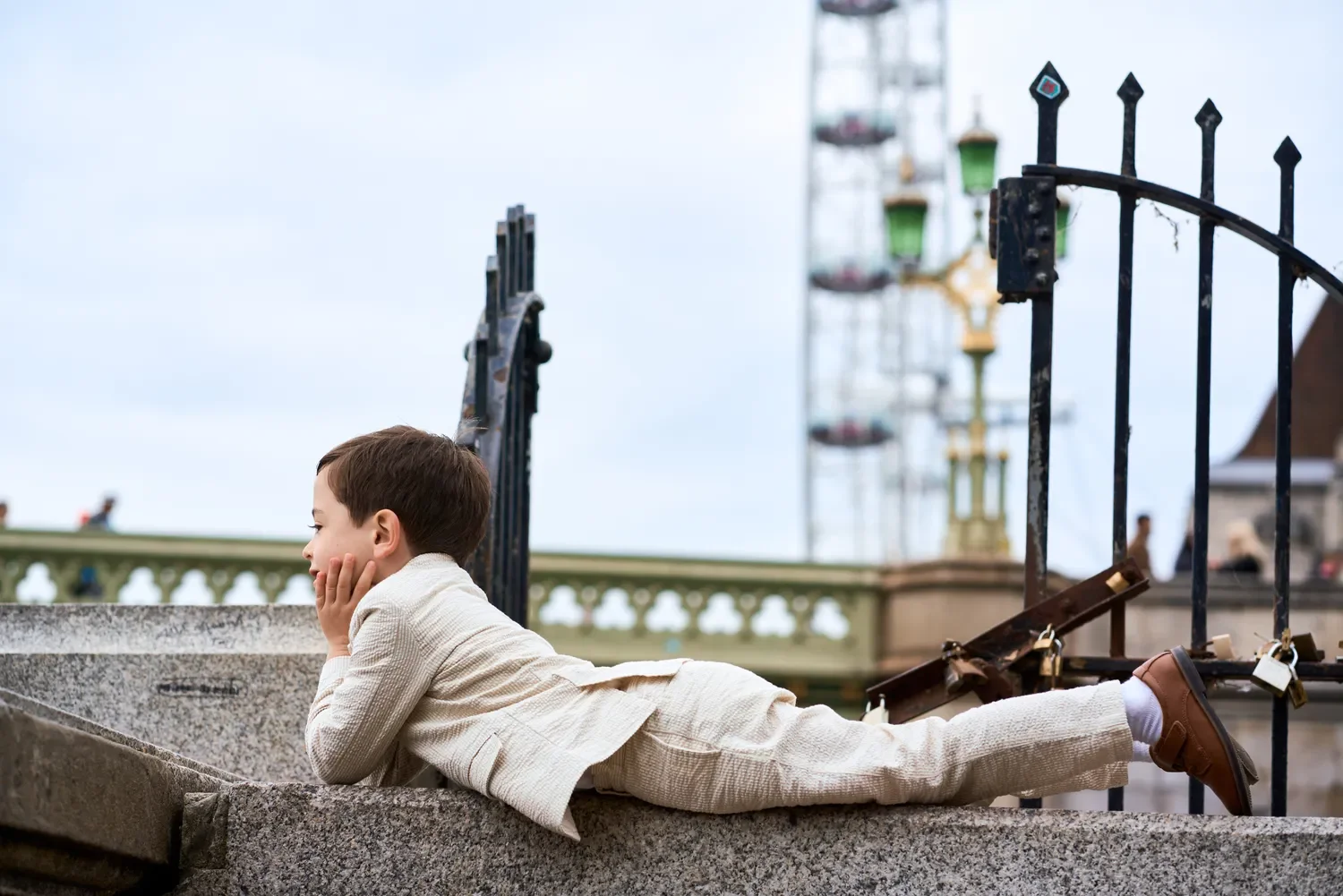 Toddler lying on Westminster Bridge wall looking at the London Eye
