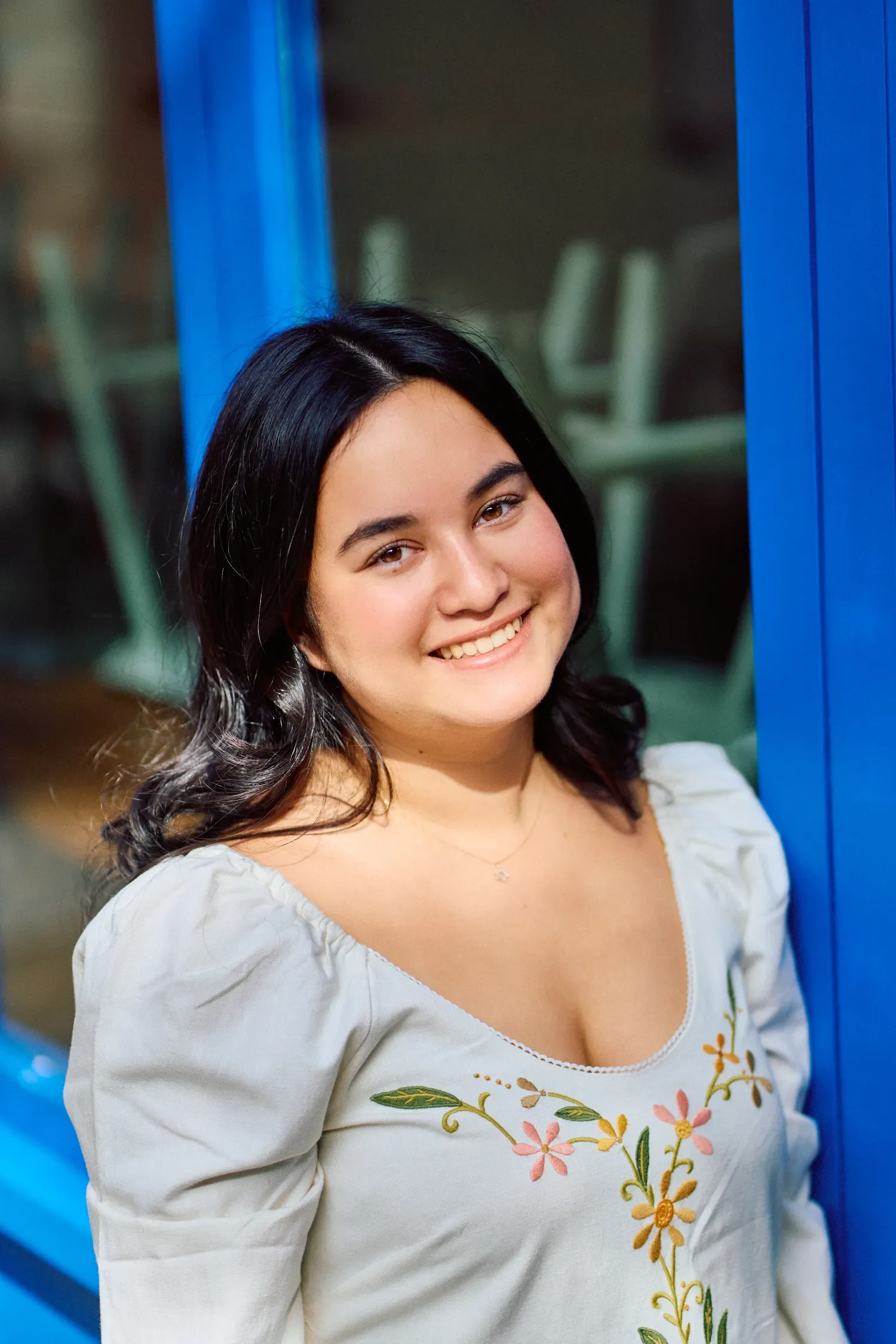 Smiling young woman in a white embroidered dress against a bright blue wall in Covent Garden