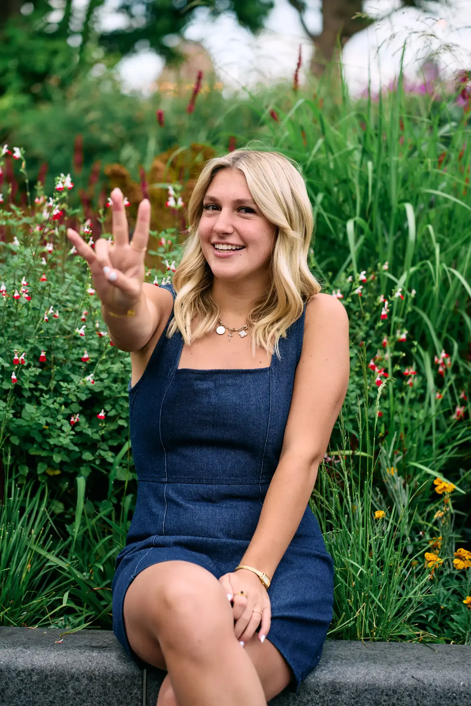 School senior portrait sitting among flowers on South Bank, giving a peace sign