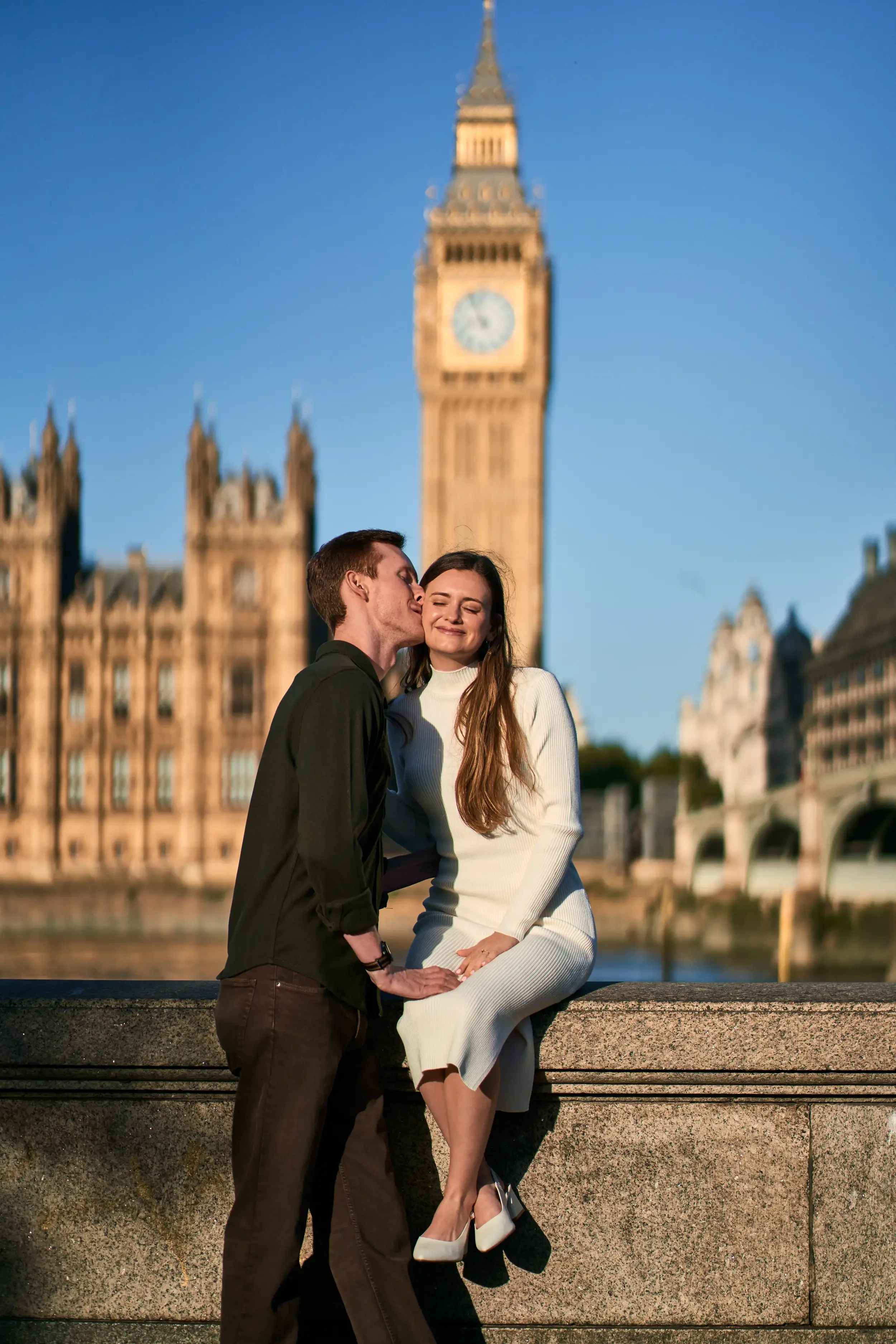 Couple seen from behind with arms around each other looking towards Big Ben and Westminster Bridge from the South Bank, London