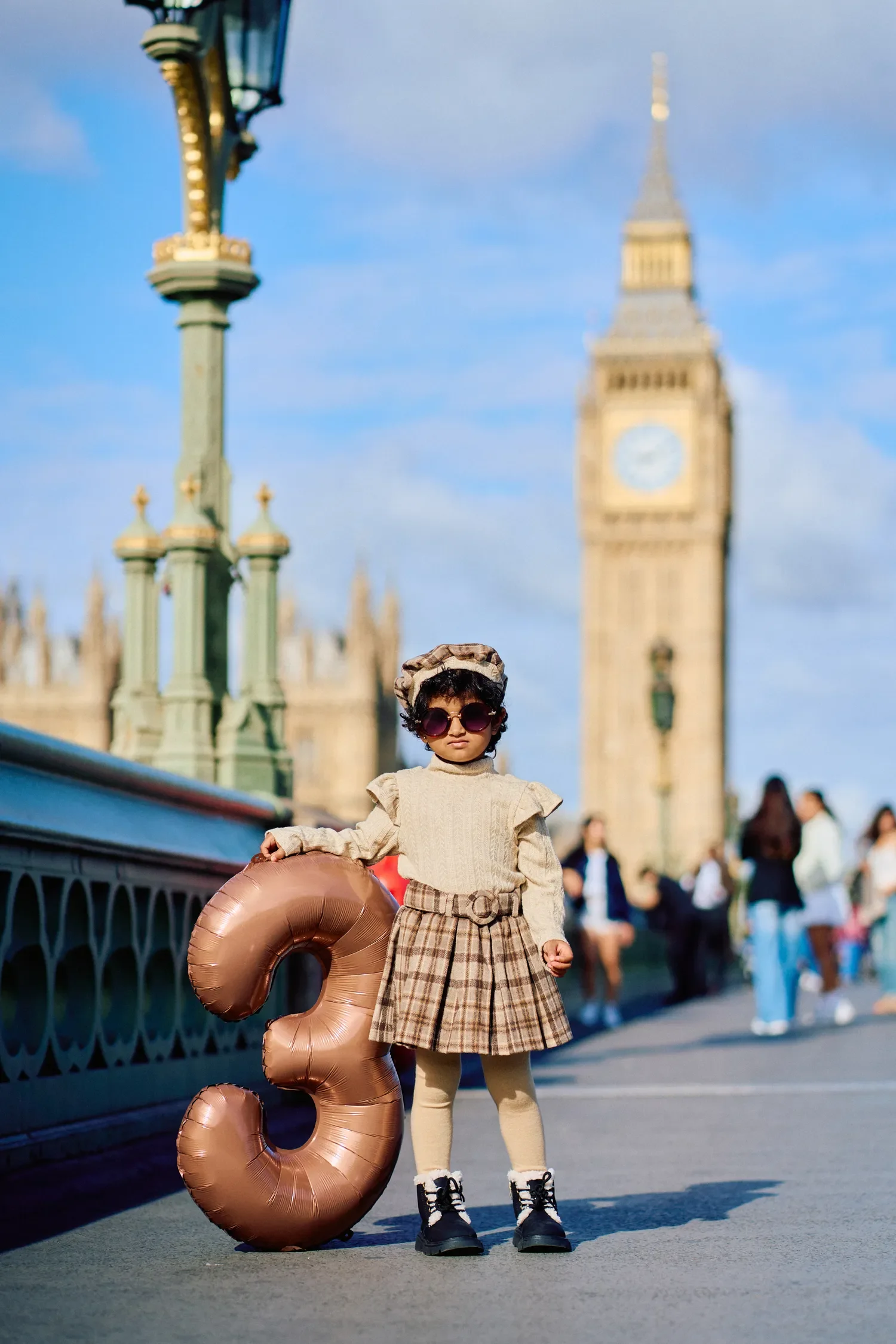 Girl in sunglasses standing beside a birthday balloon on Westminster Bridge, London
