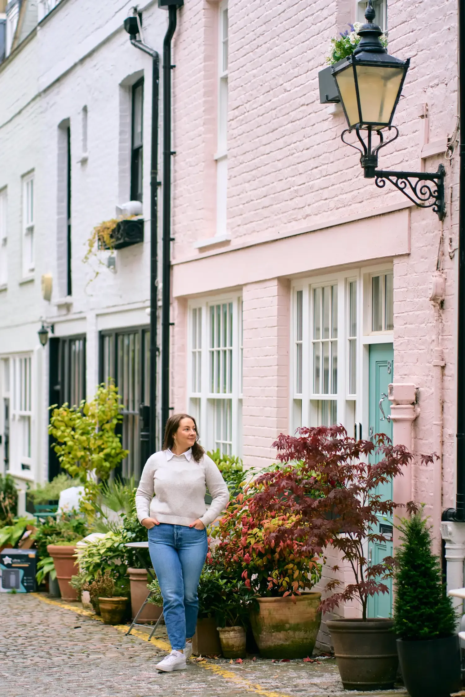 Woman in a white top and jeans outside a pink mews house in Kensington