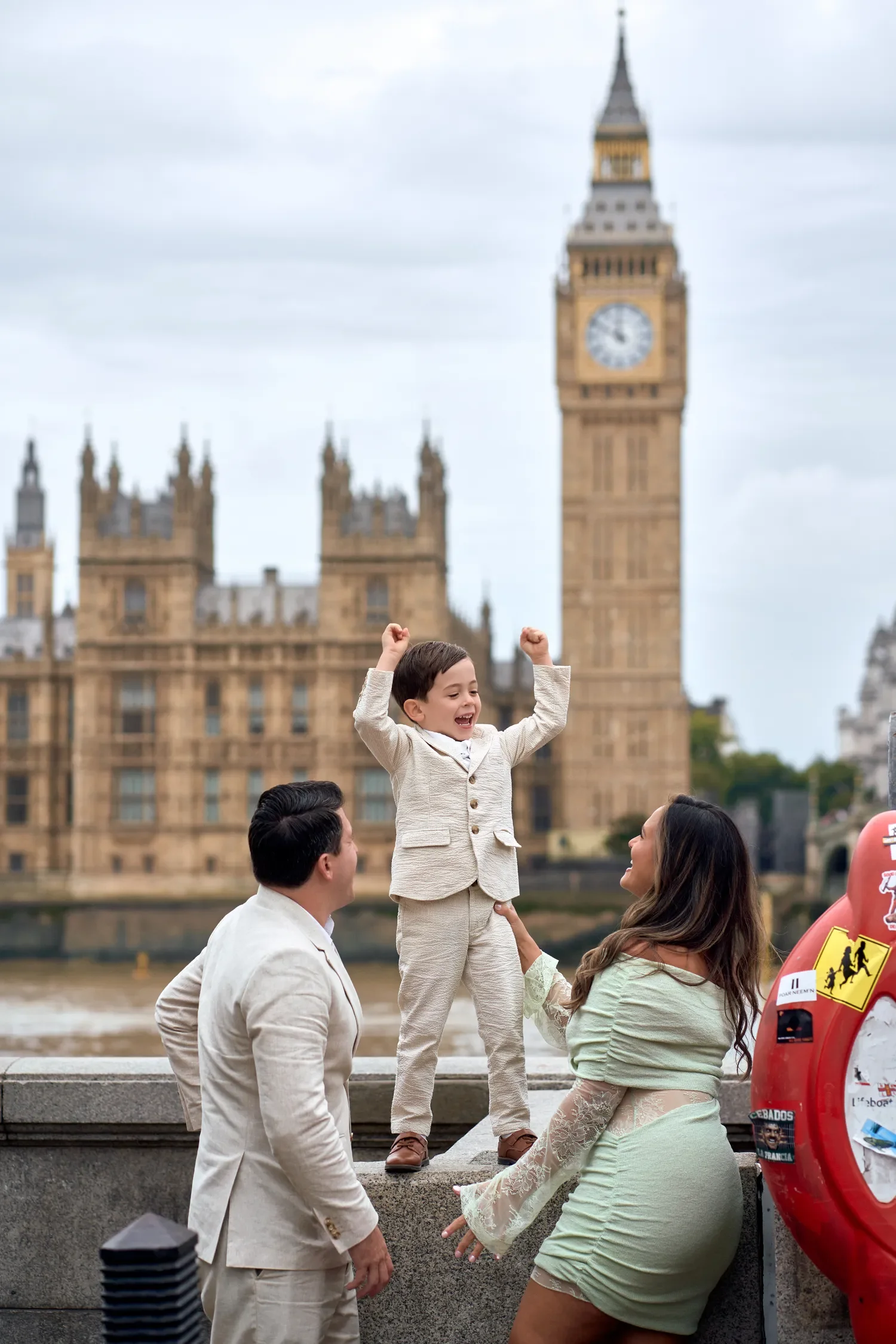 Father lifting toddler in the air on Westminster Bridge, Houses of Parliament in view
