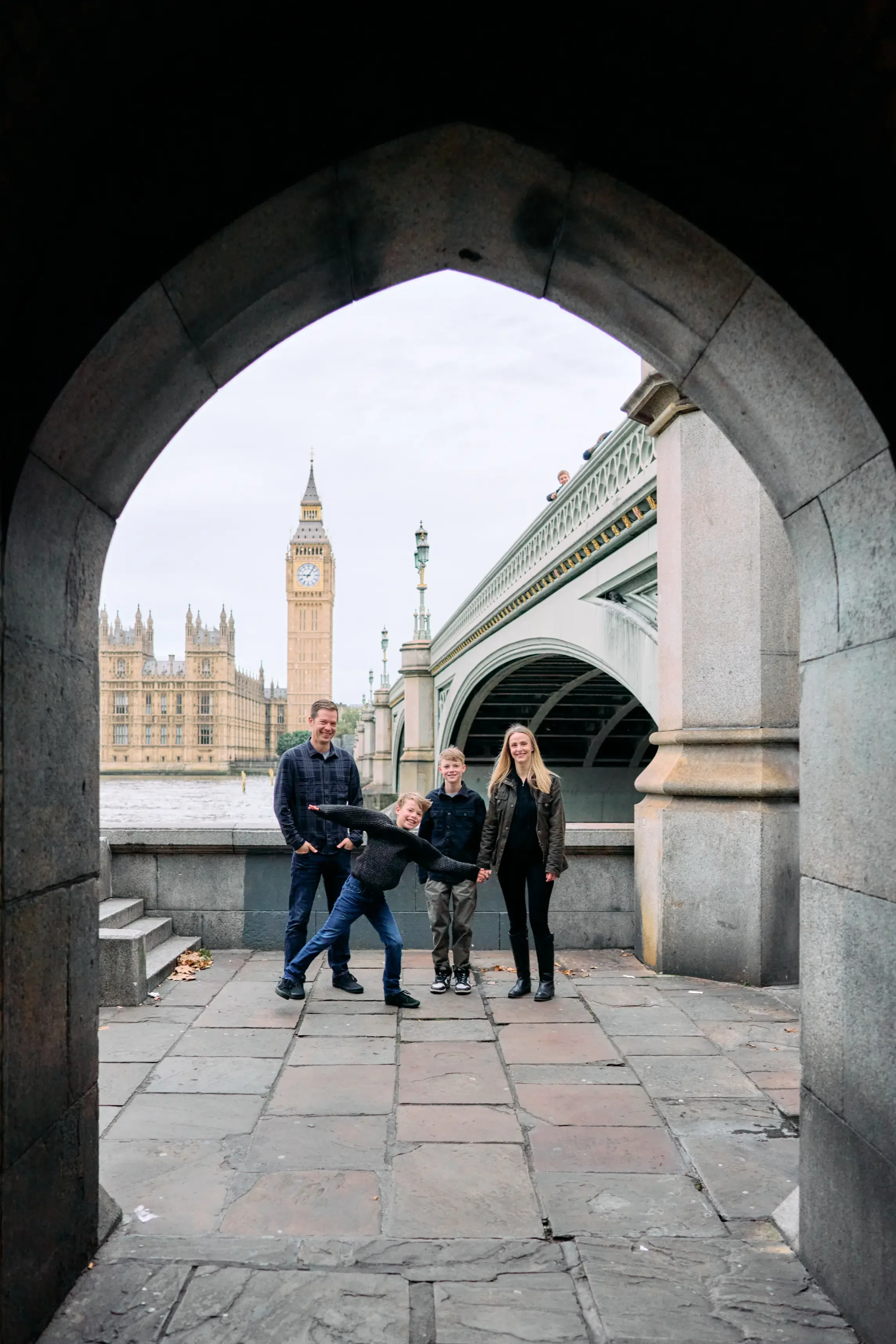 Family of four framed by a stone archway on the South Bank with Big Ben and Westminster Bridge in the background during a London family photoshoot