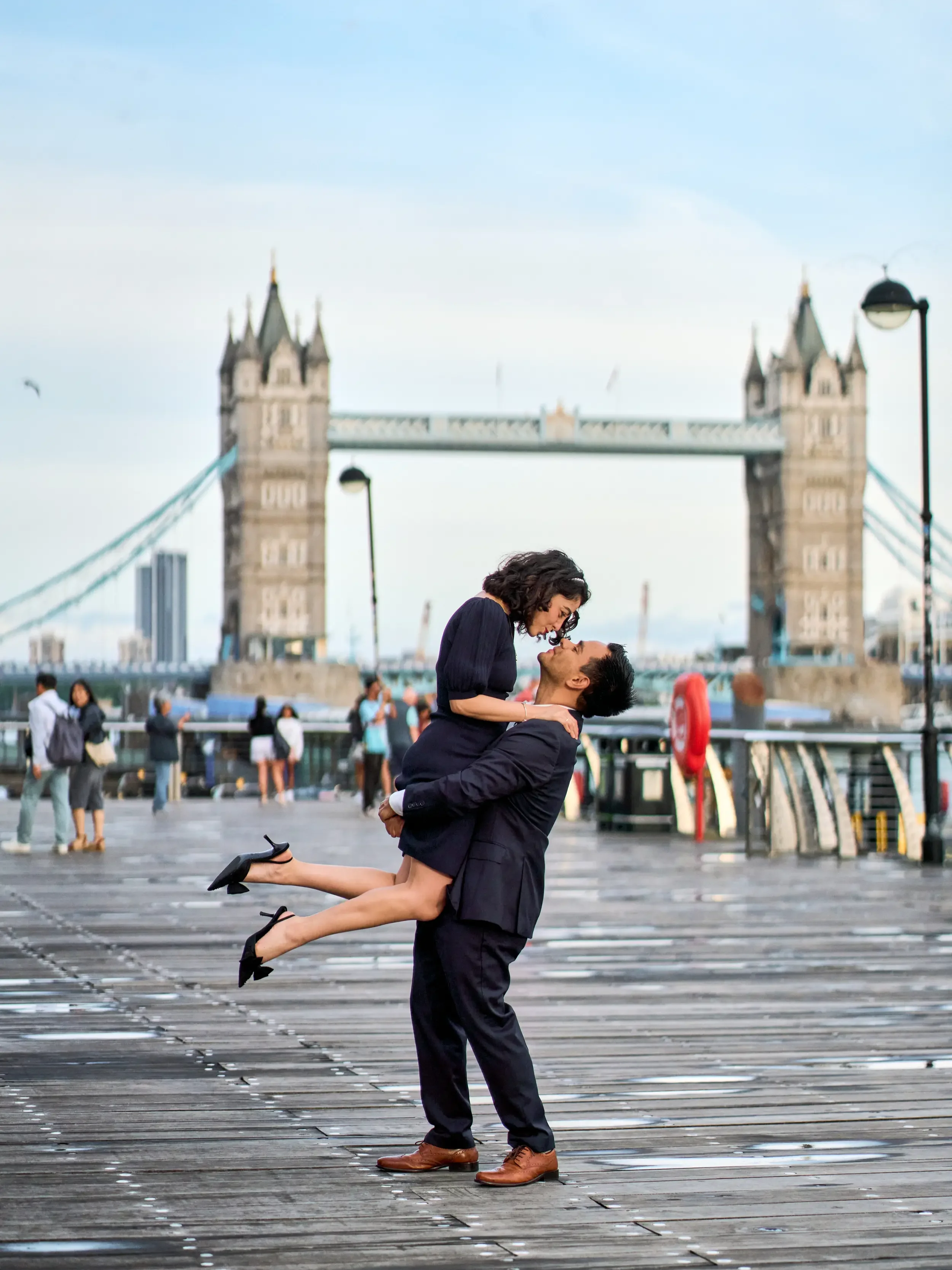 Man lifting his partner in the air with Tower Bridge in the background during an engagement photoshoot in London