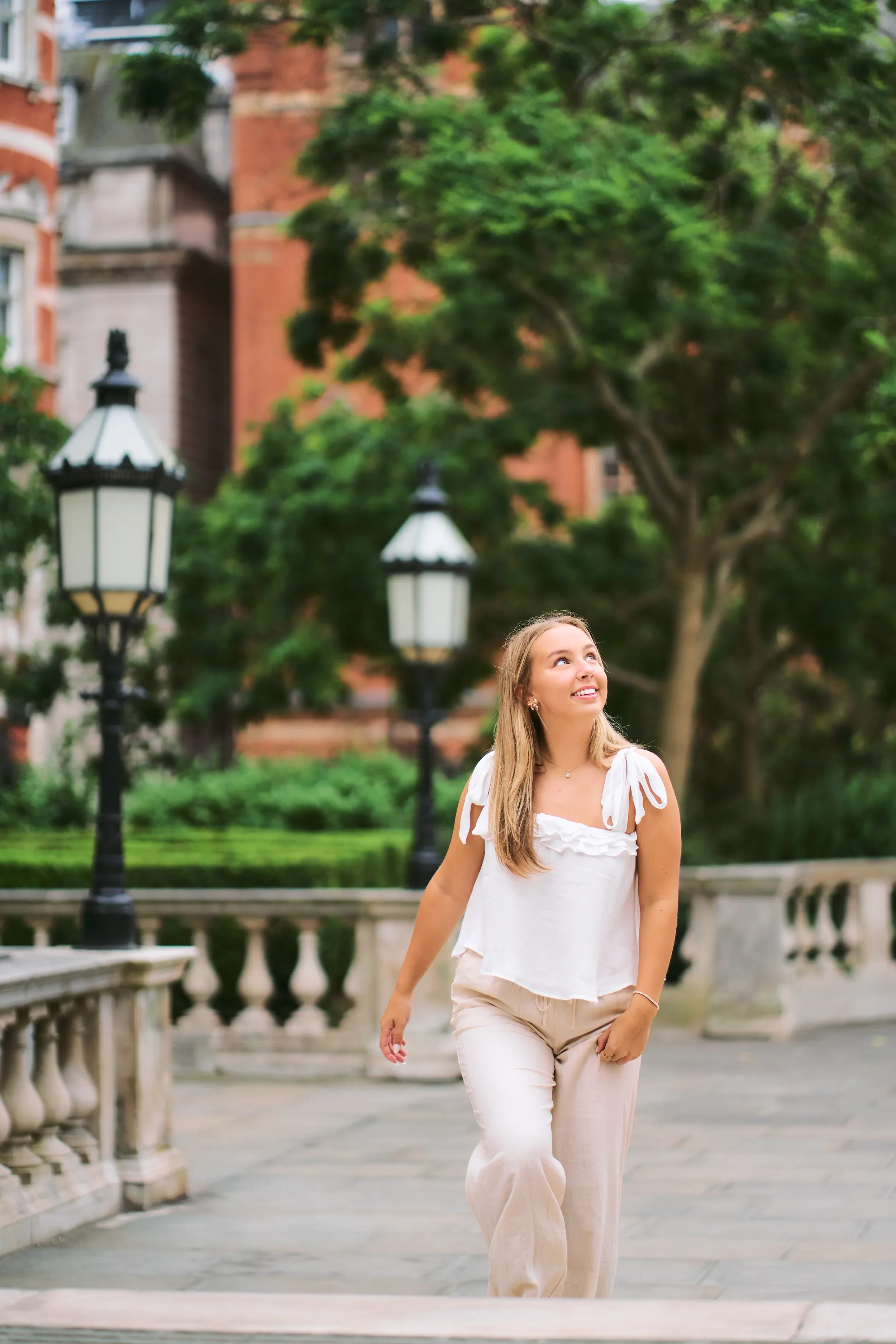 High school senior walking and looking up on a terrace with heritage lampposts and balustrades in Kensington, London