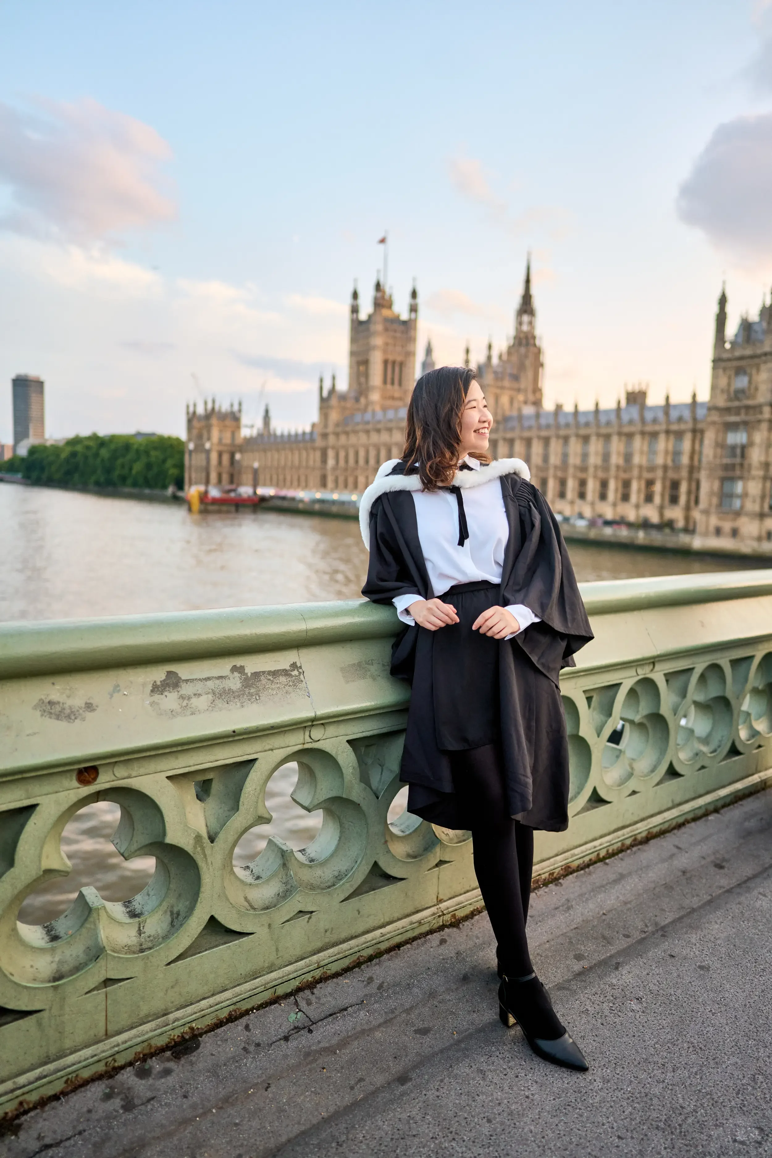 Graduate in cap and gown on Westminster Bridge with the Houses of Parliament behind