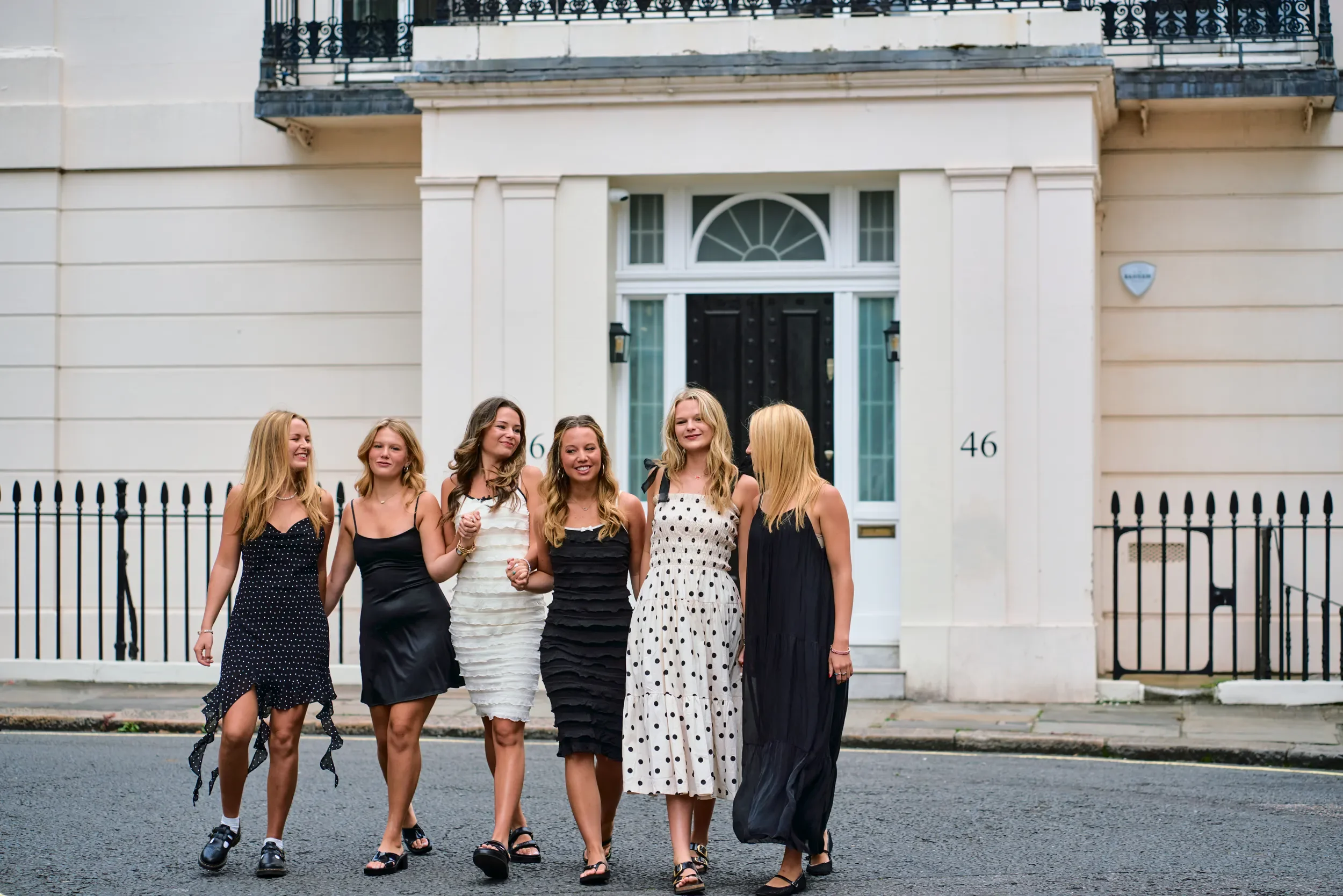 Group of friends in black and white dresses walking arm in arm past a cream townhouse in London — what to wear for a group photoshoot