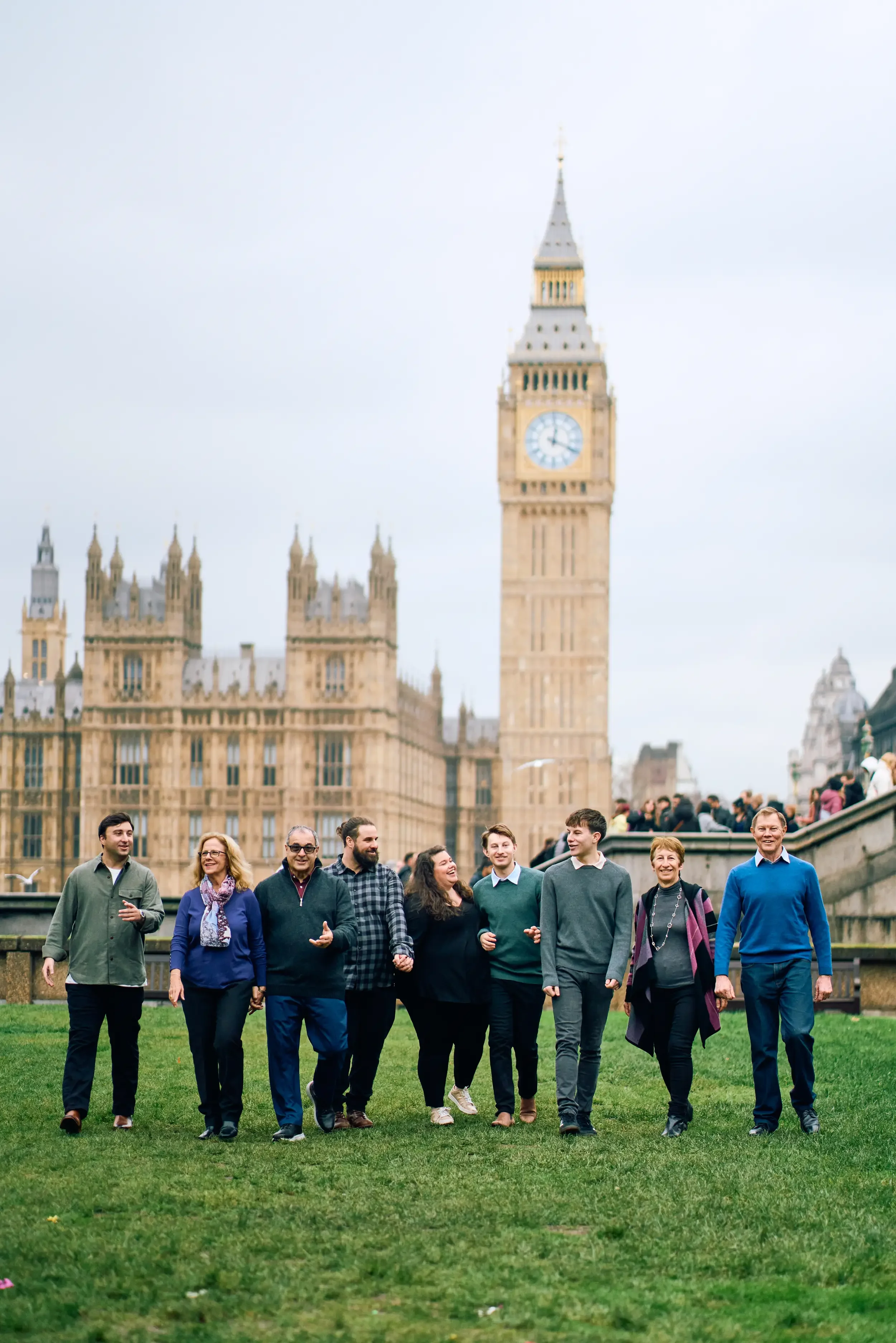 Large extended family walking and laughing together on the grass with Big Ben and the Houses of Parliament behind them during a family photoshoot in London