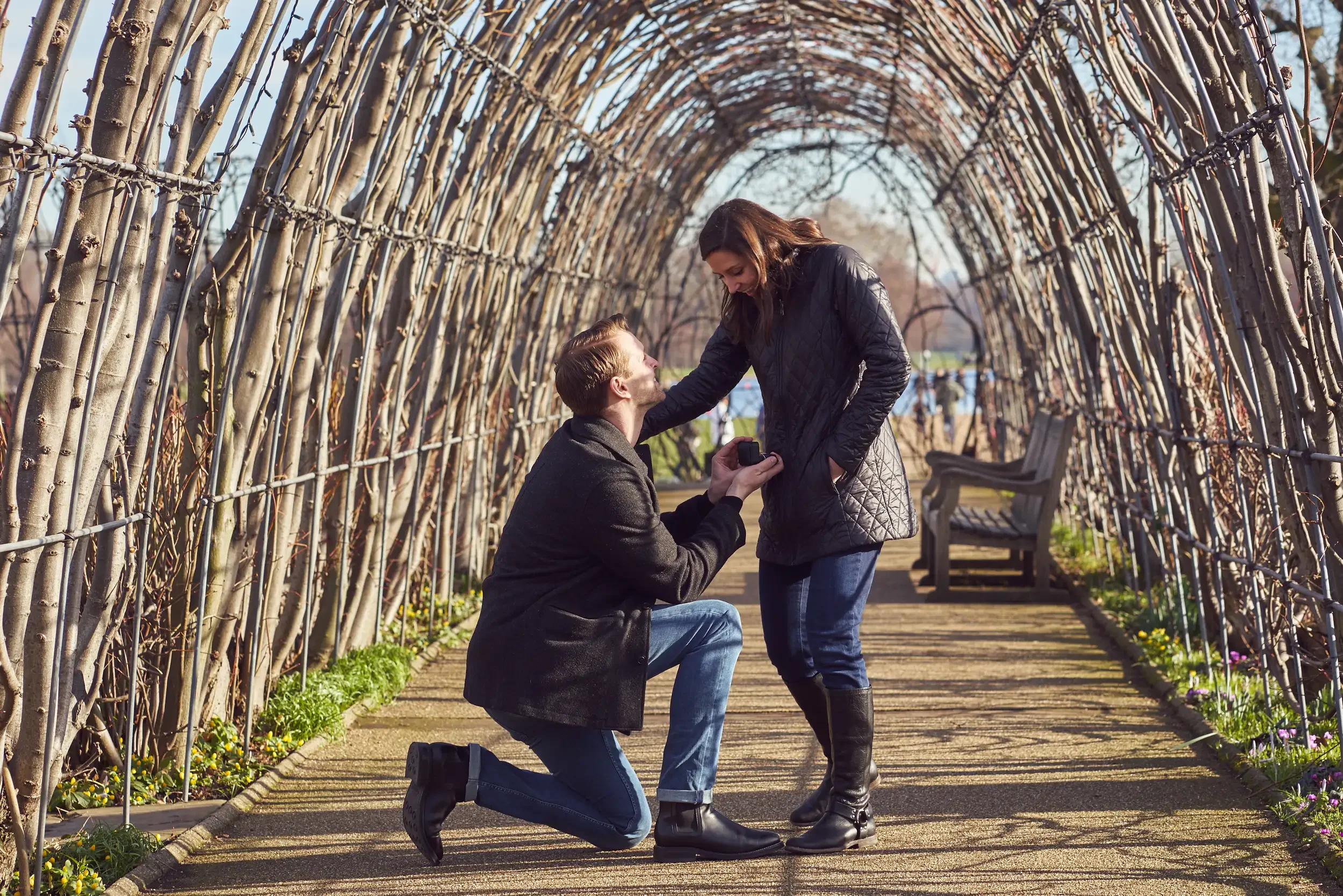 Man proposing on one knee under a winter garden archway in Kensington Gardens, London