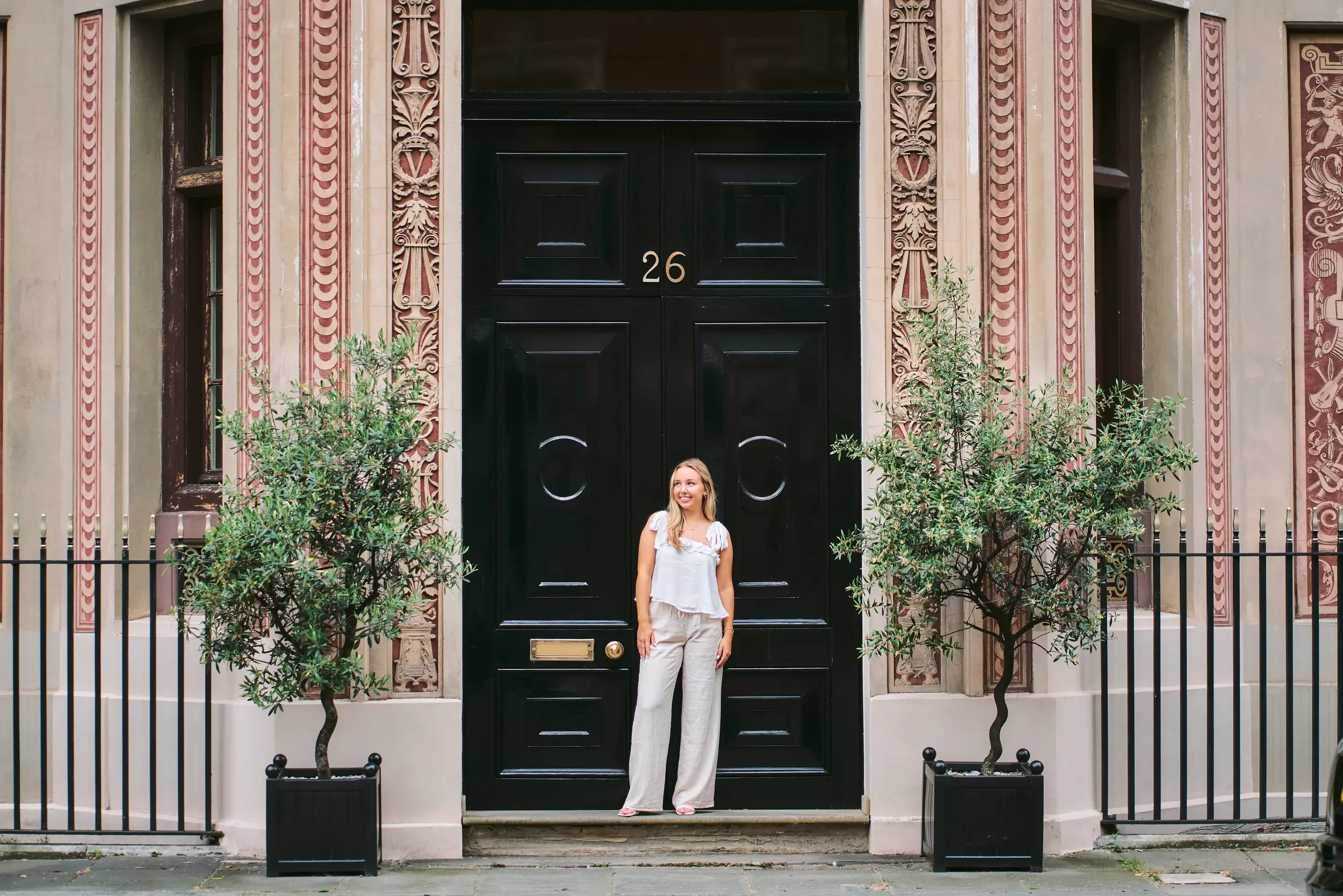 Full-length high school senior portrait in front of a grand red brick Victorian mansion in Kensington, London