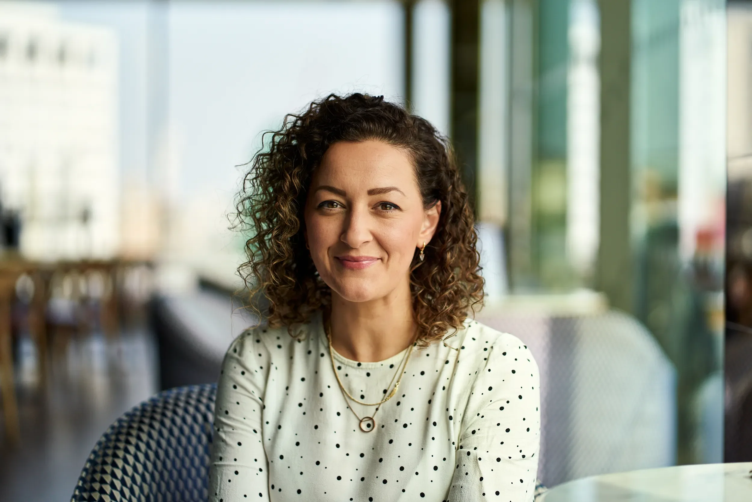 Woman with curly hair in a green polka dot top outside a cafe in Soho, London