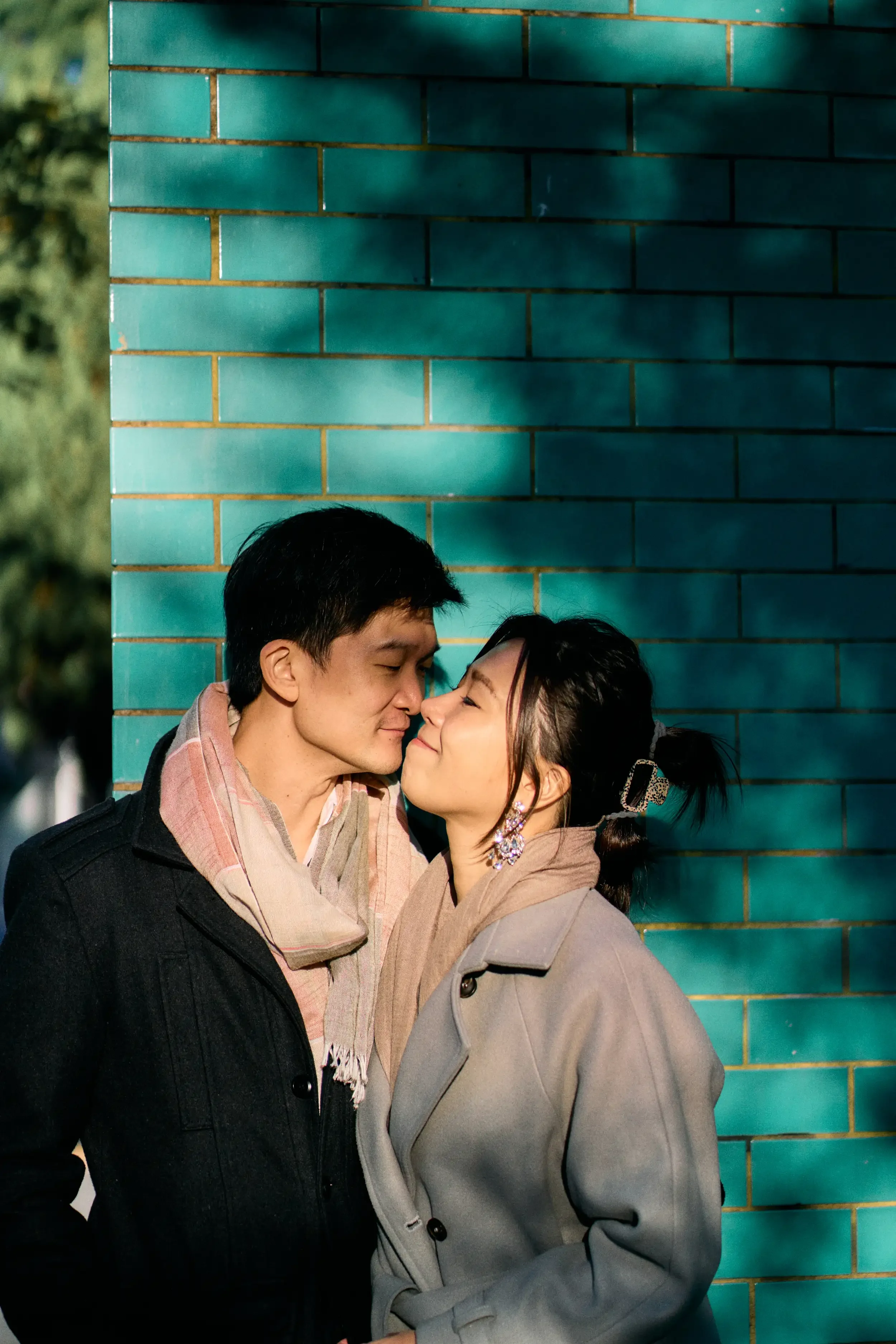 Couple sharing a kiss against teal glazed brick wall during a couples photoshoot in Notting Hill, London - Tepewehco Photography by Kate