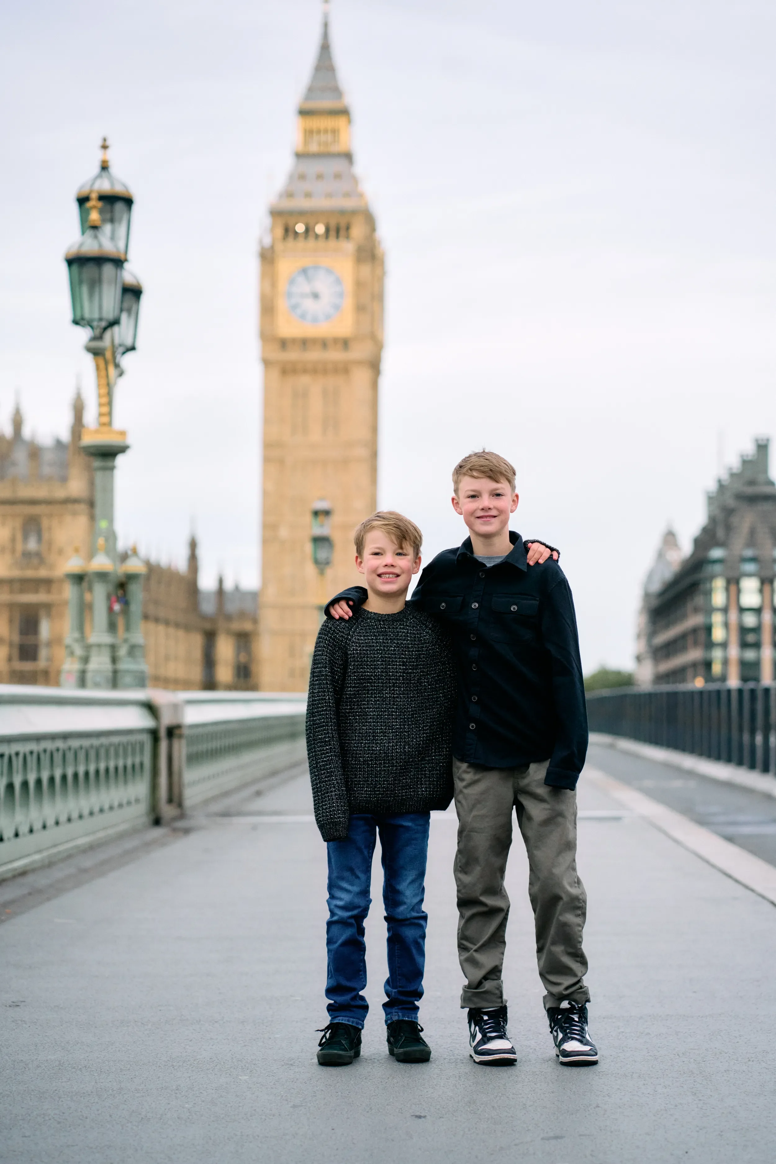 Two brothers with arms around each other on Westminster Bridge with Big Ben in the background during a family photoshoot in London