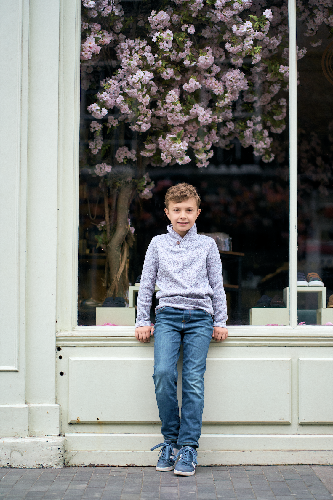 Young boy standing in front of a cherry blossom shopfront window on a Belgravia street