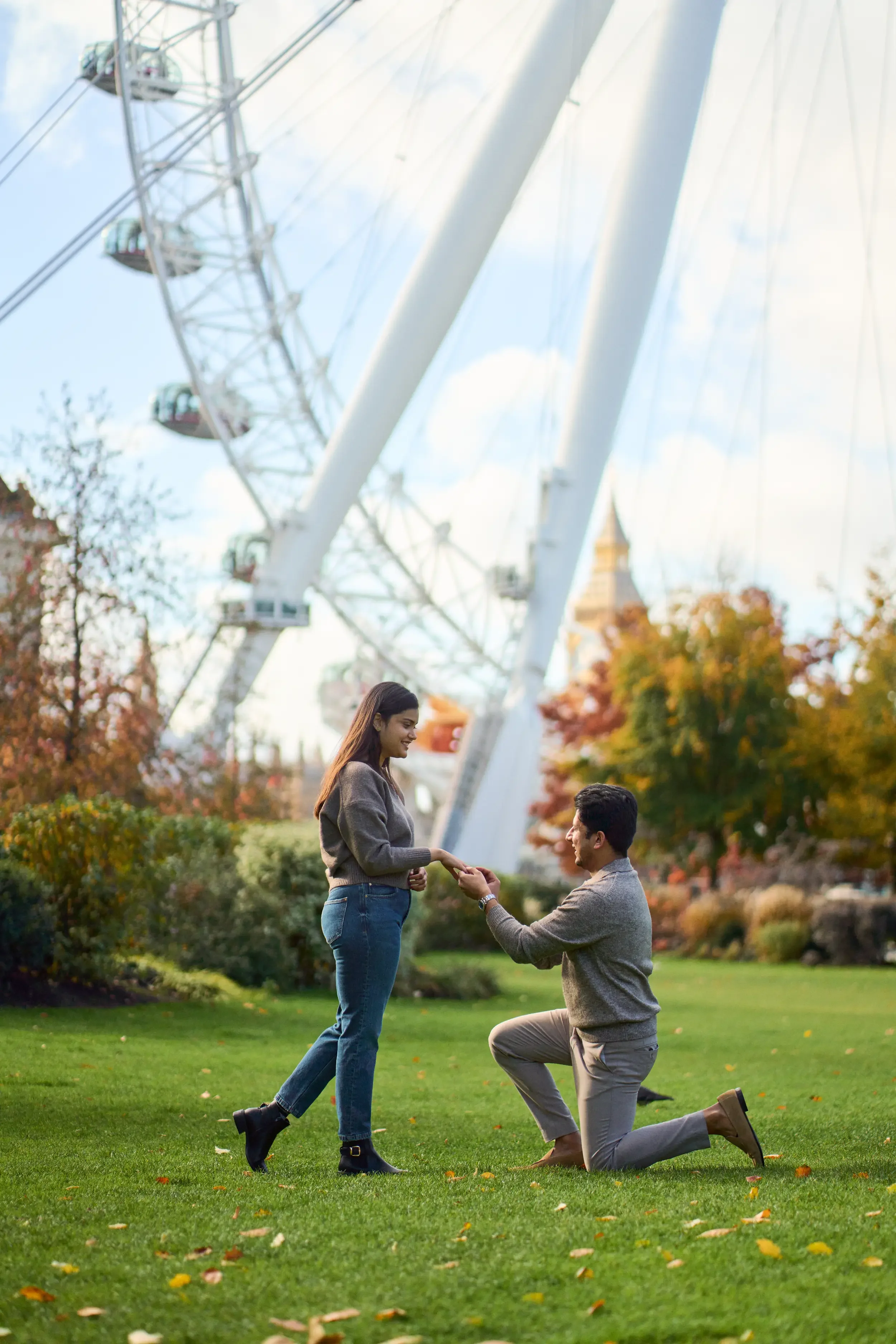 Man proposing on one knee on the grass with the London Eye and autumn leaves in the background, South Bank, London