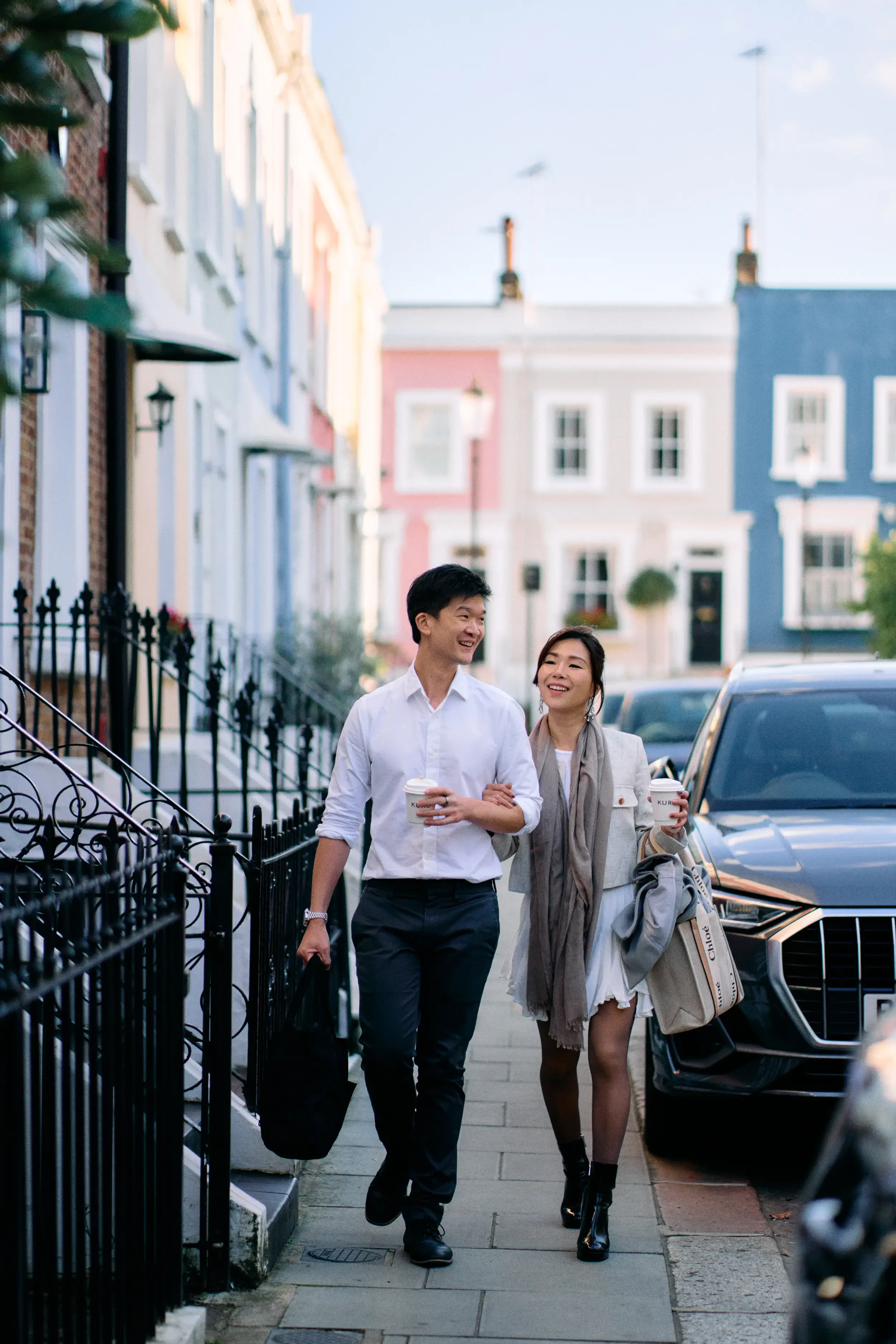 Couple walking arm in arm with coffee cups along a colourful Notting Hill street lined with pastel Victorian houses, London - Tepewehco Photography by Kate