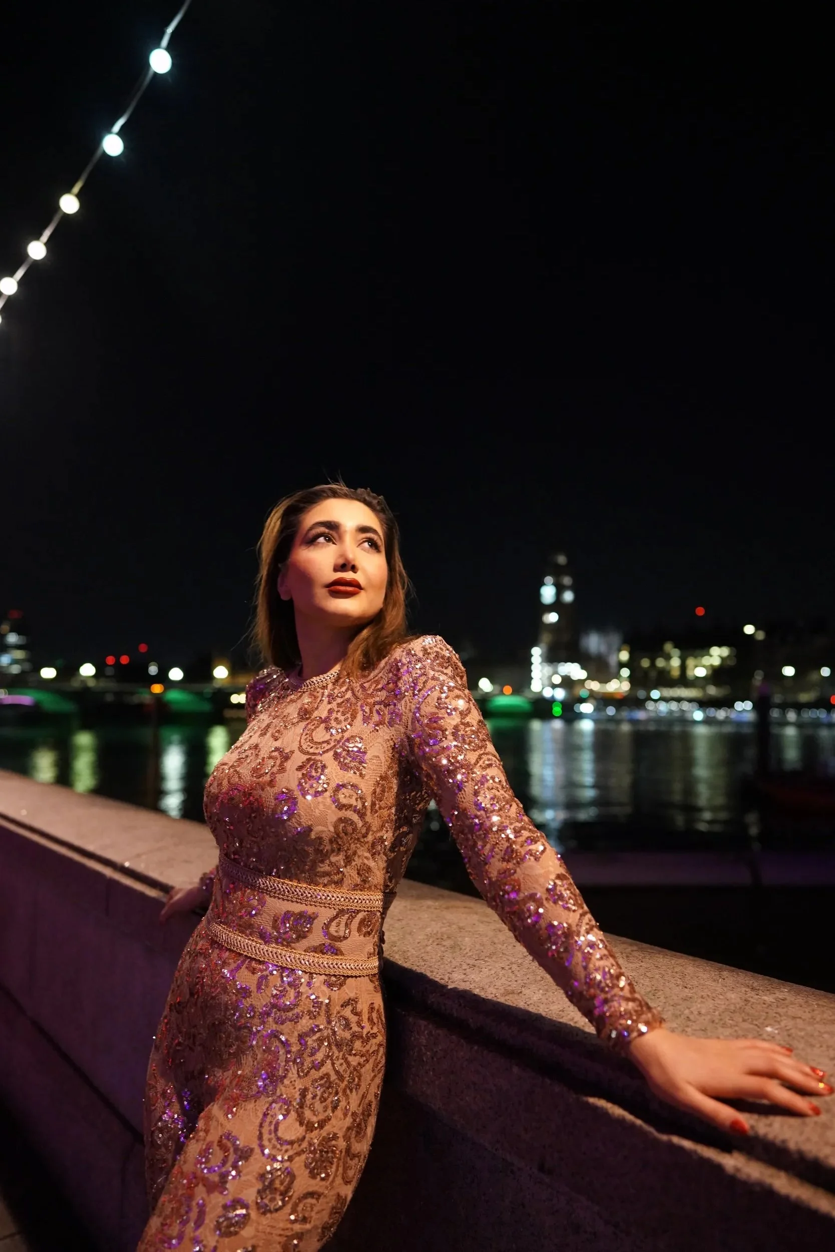 Night portrait of a woman in a sequin dress on the South Bank with city lights reflecting on the Thames, London