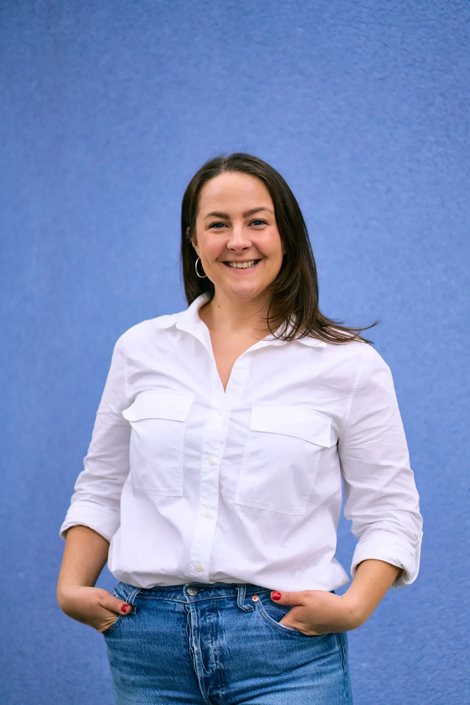 Personal brand portrait of a woman in a white shirt and jeans against a blue backdrop