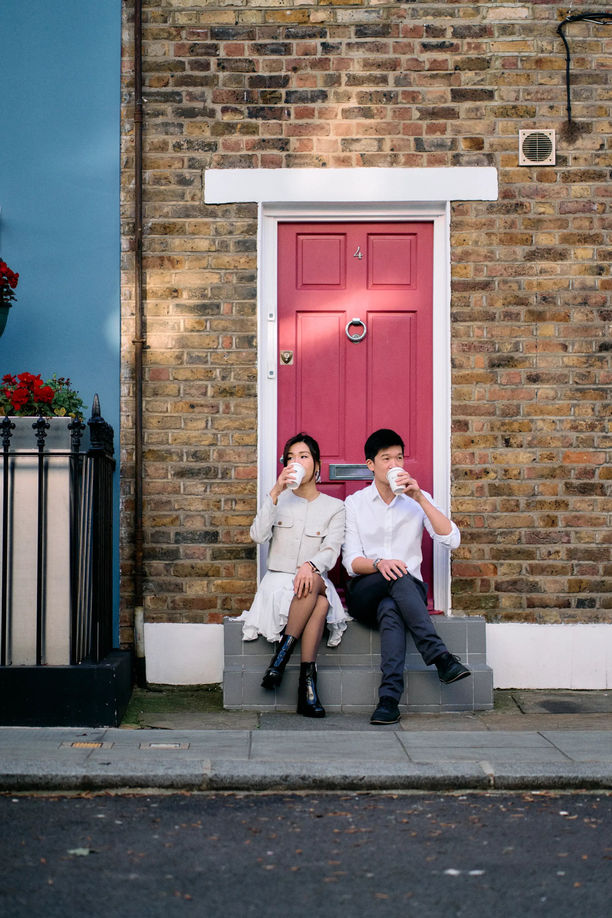 Couple sitting on a doorstep drinking coffee in front of a red door and brick wall in Notting Hill, London - Tepewehco Photography by Kate