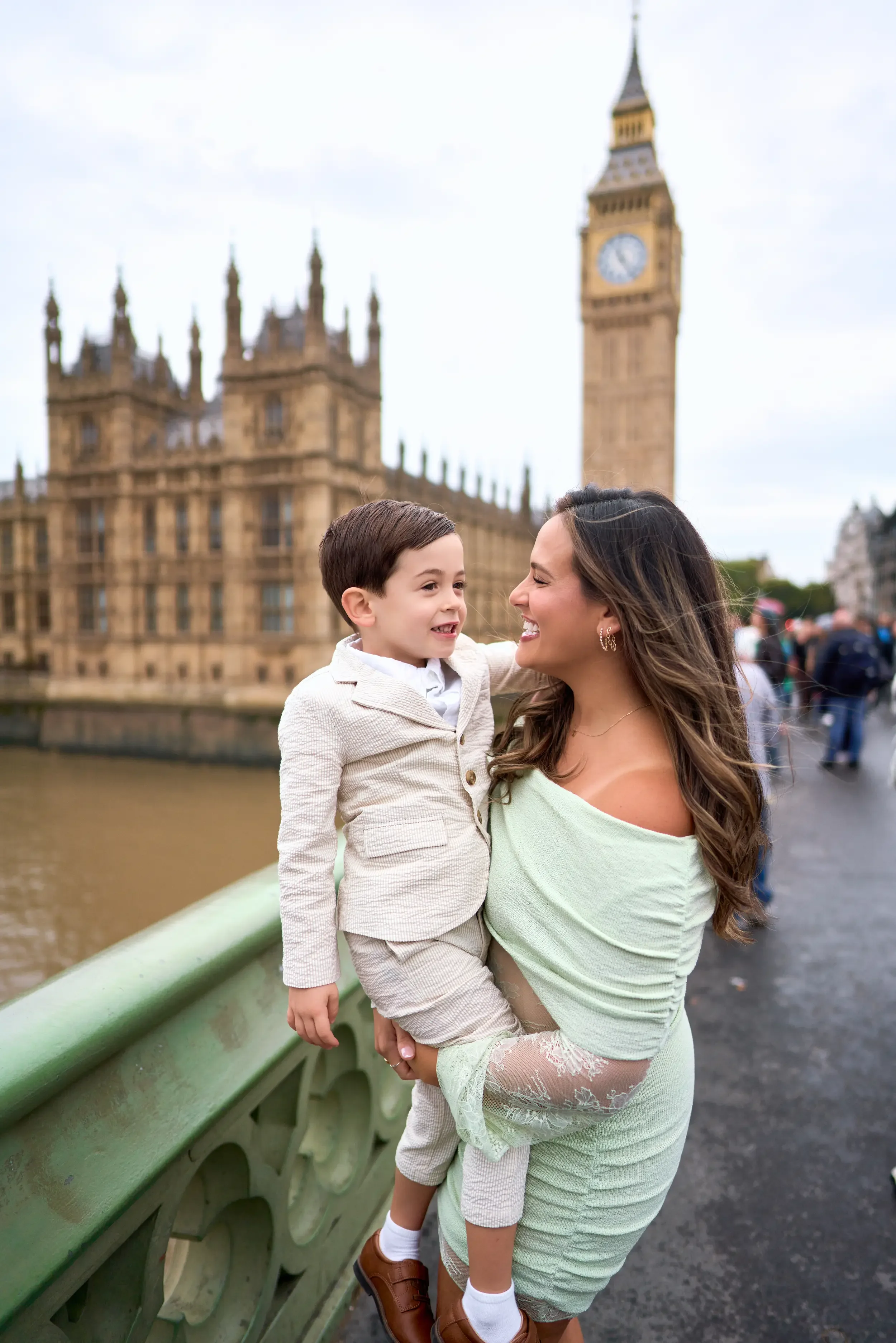 Mother and young son smiling at each other on Westminster Bridge with Big Ben and the Houses of Parliament behind them during a family photoshoot in London