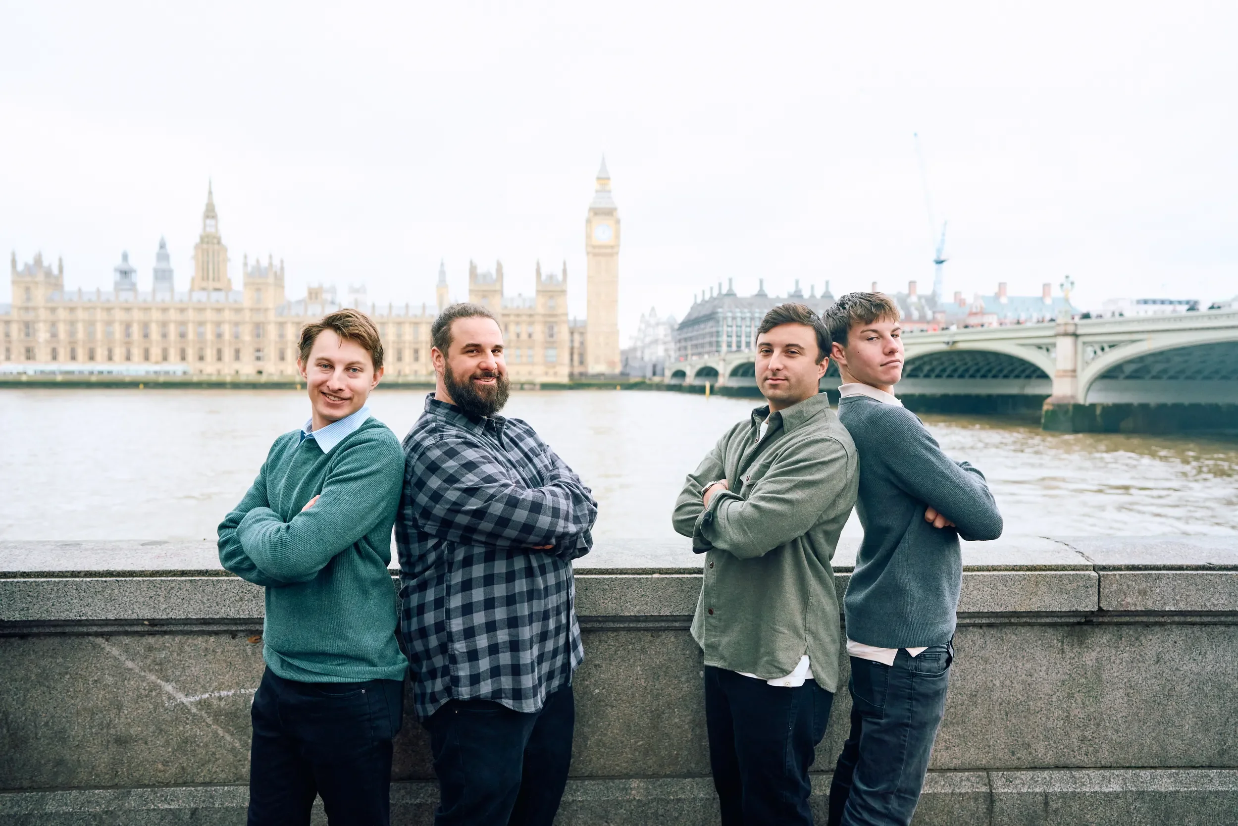 Four friends standing back to back with arms crossed on the South Bank with Big Ben and Westminster Bridge in the background, London