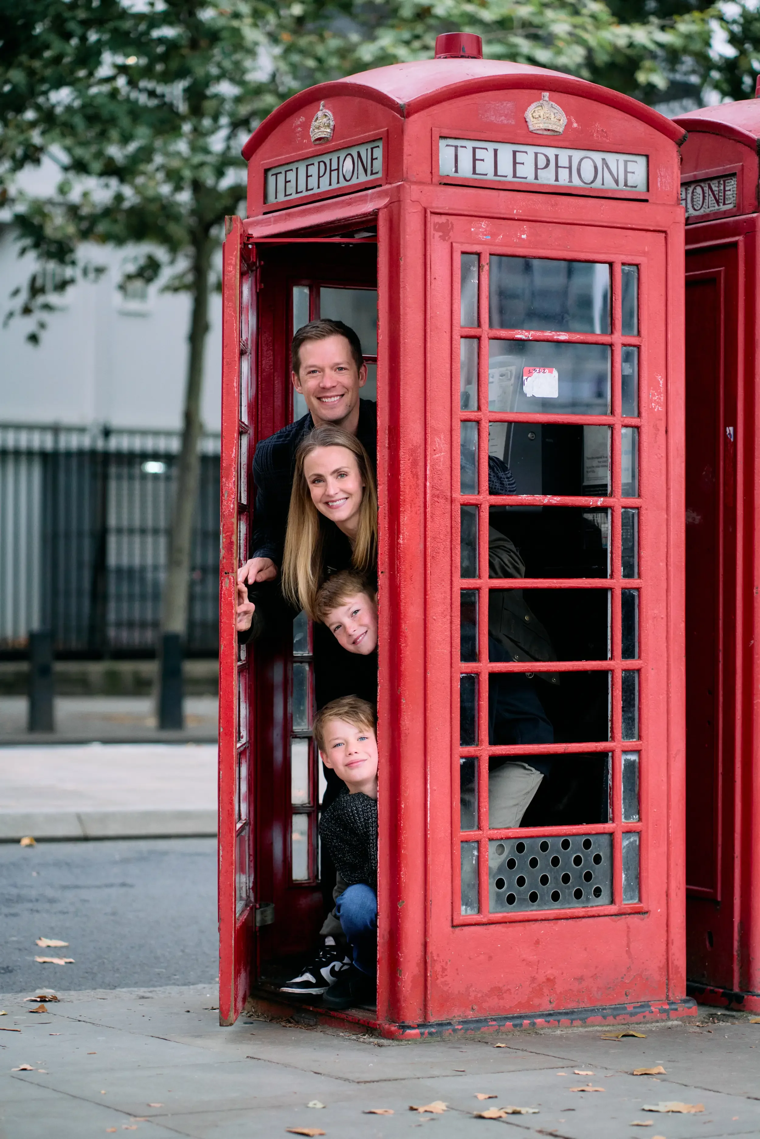 Family of four peeking out of a red London telephone box stacked on top of each other during a fun family photoshoot in London