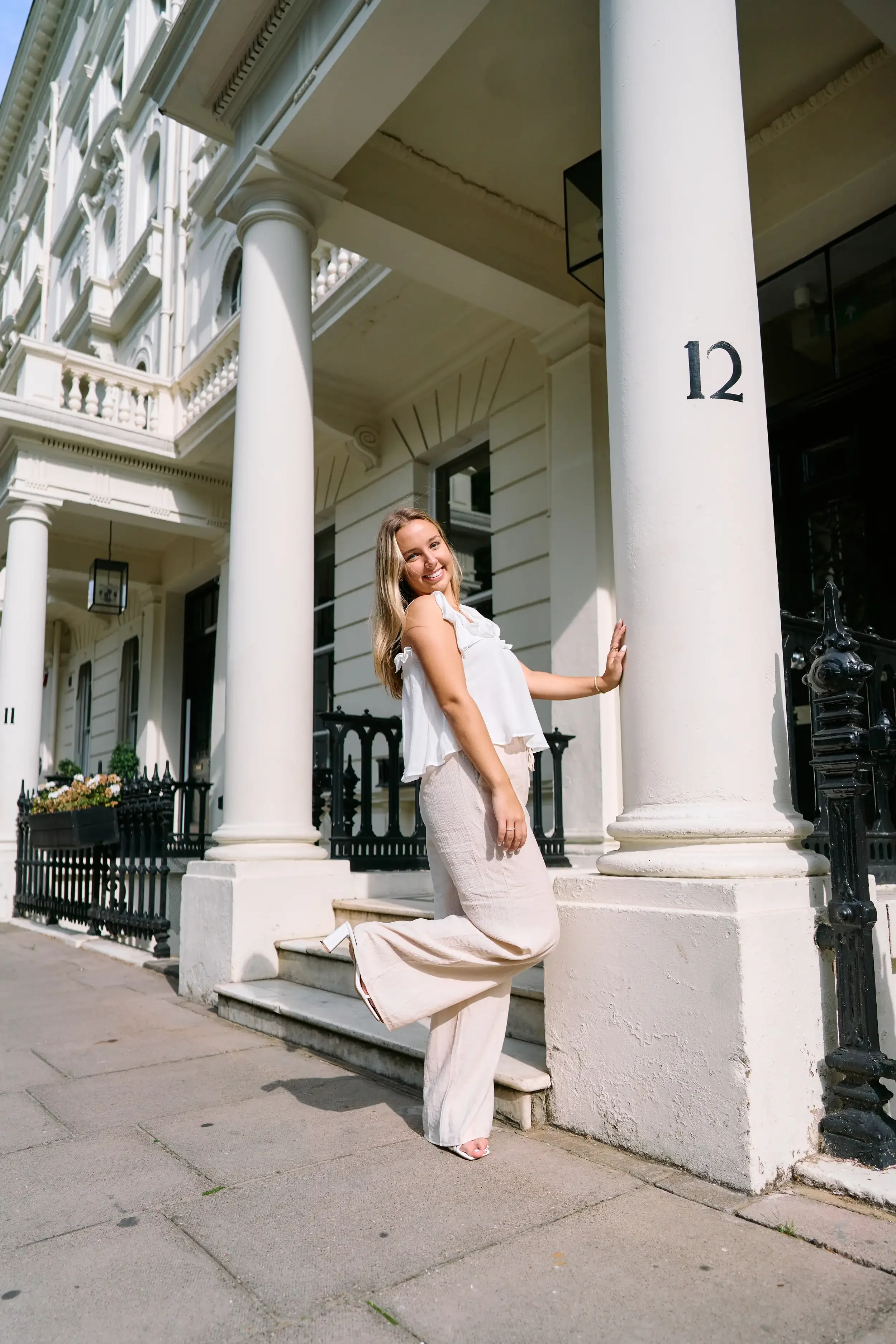 High school senior leaning playfully against a white column at a grand Kensington townhouse entrance, London