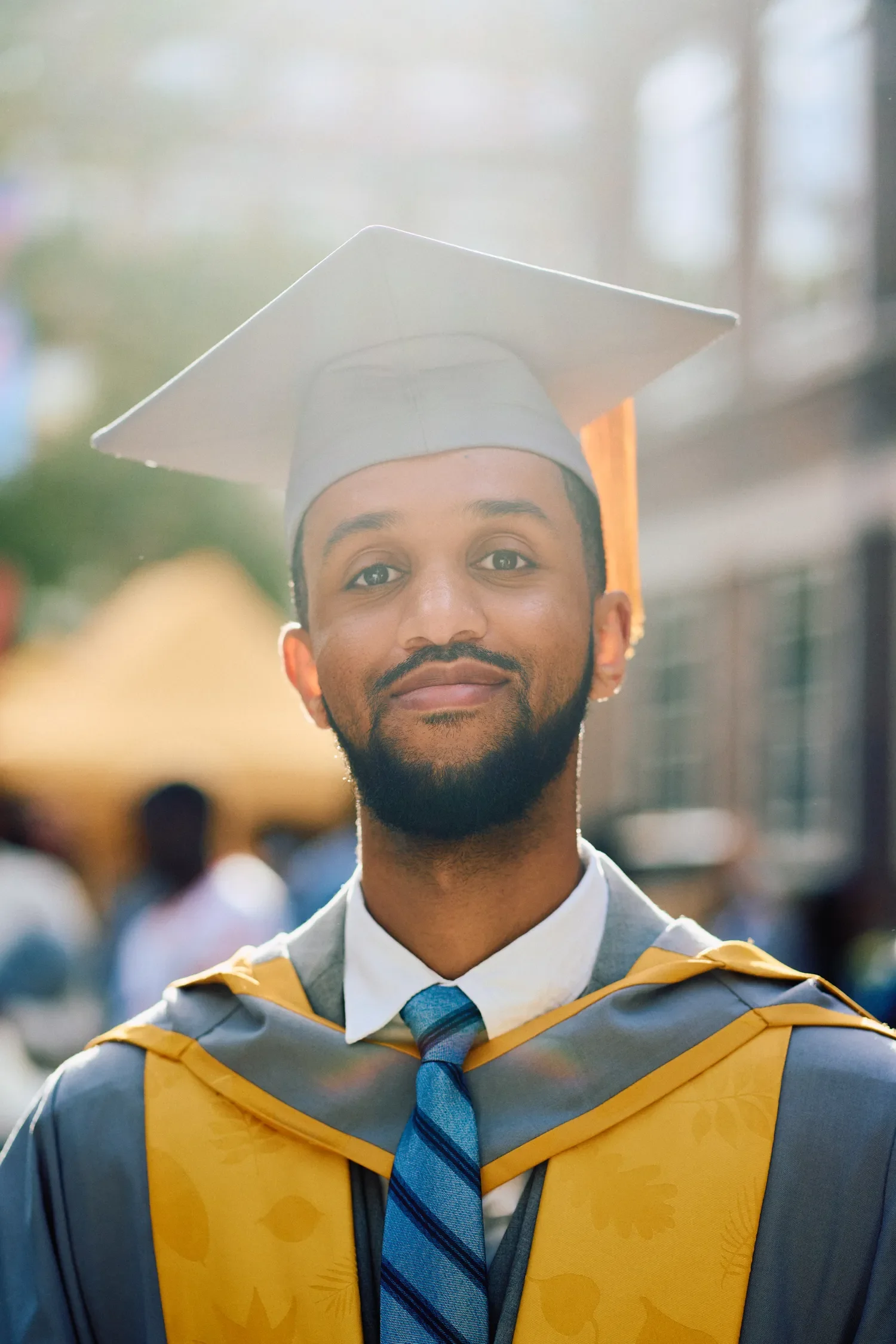 Male graduate in cap and gown smiling outdoors in Russell Square, London