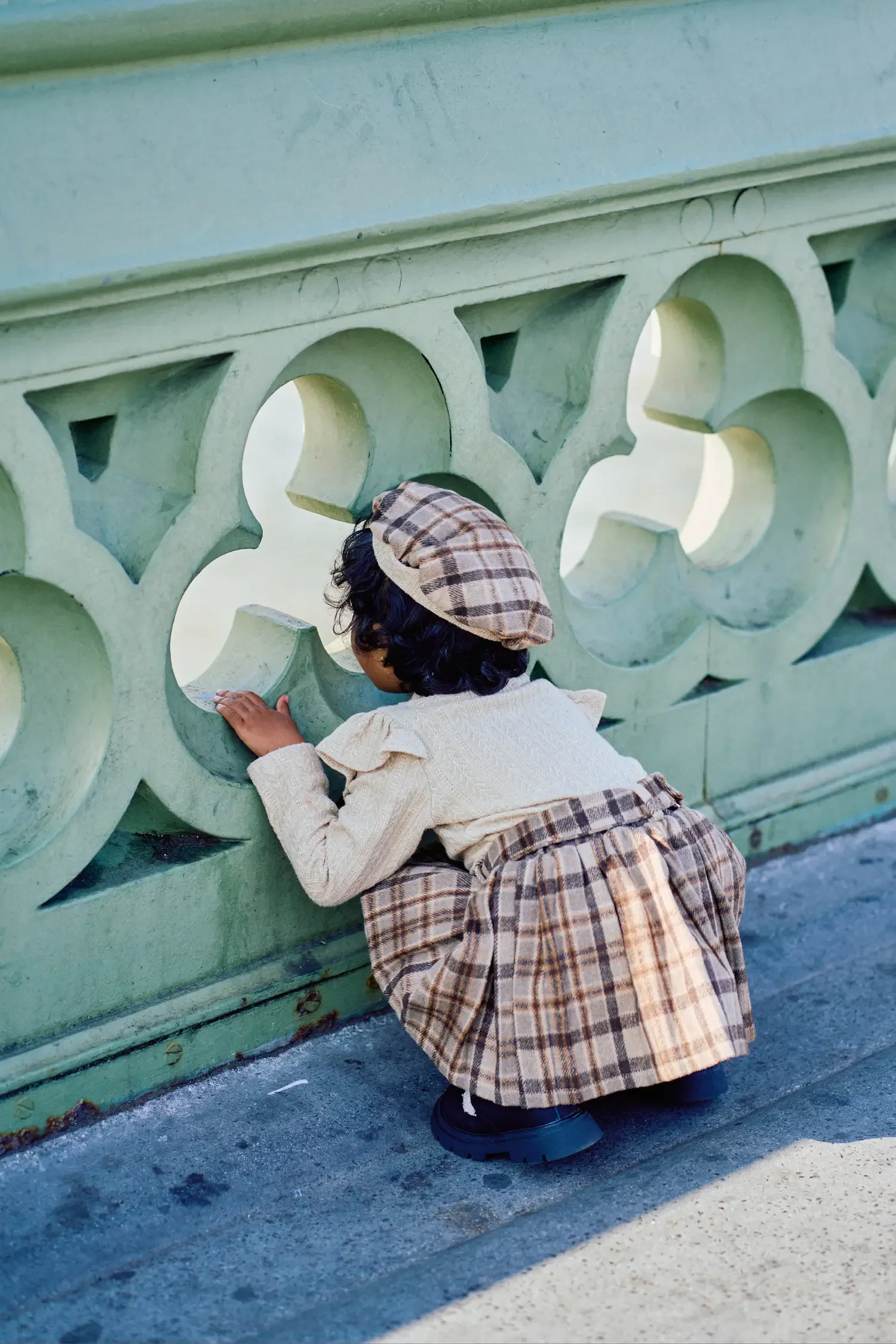 Toddler girl crouching by Westminster Bridge stonework during family photoshoot