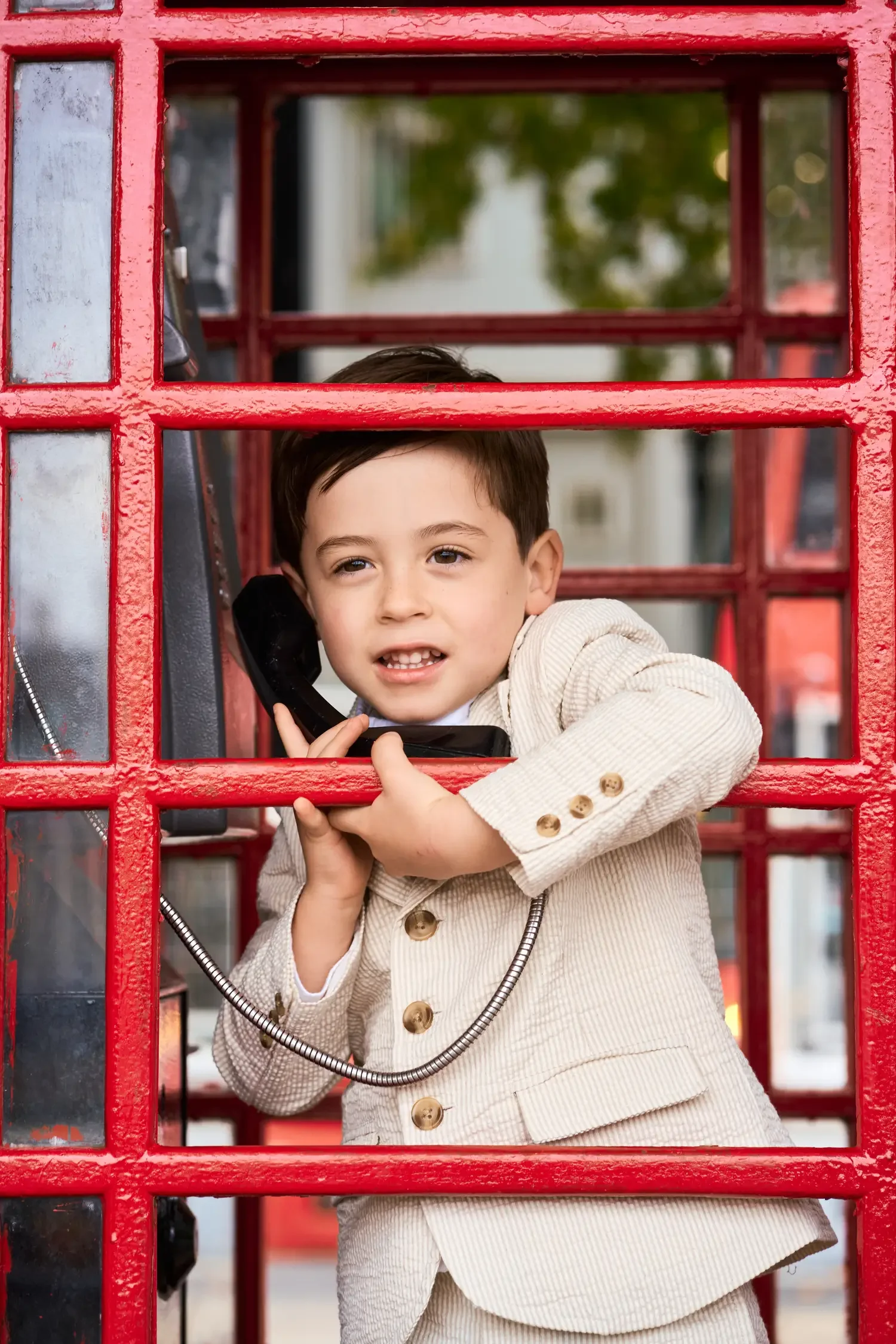 Toddler boy pretending to use the phone in a red London phone box